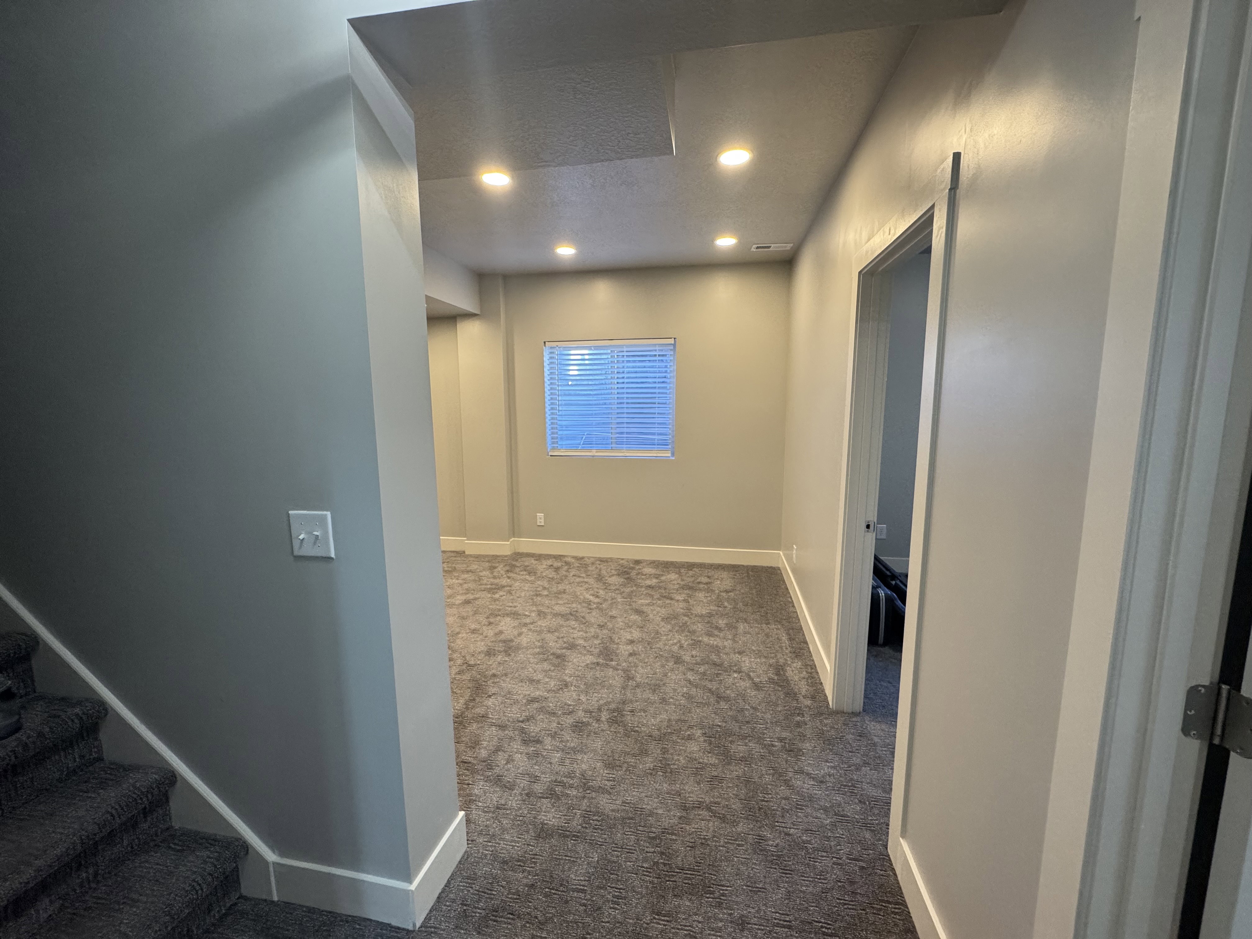 Finished lower-level space featuring recessed lighting, a window with blinds, and neutral grey carpeting