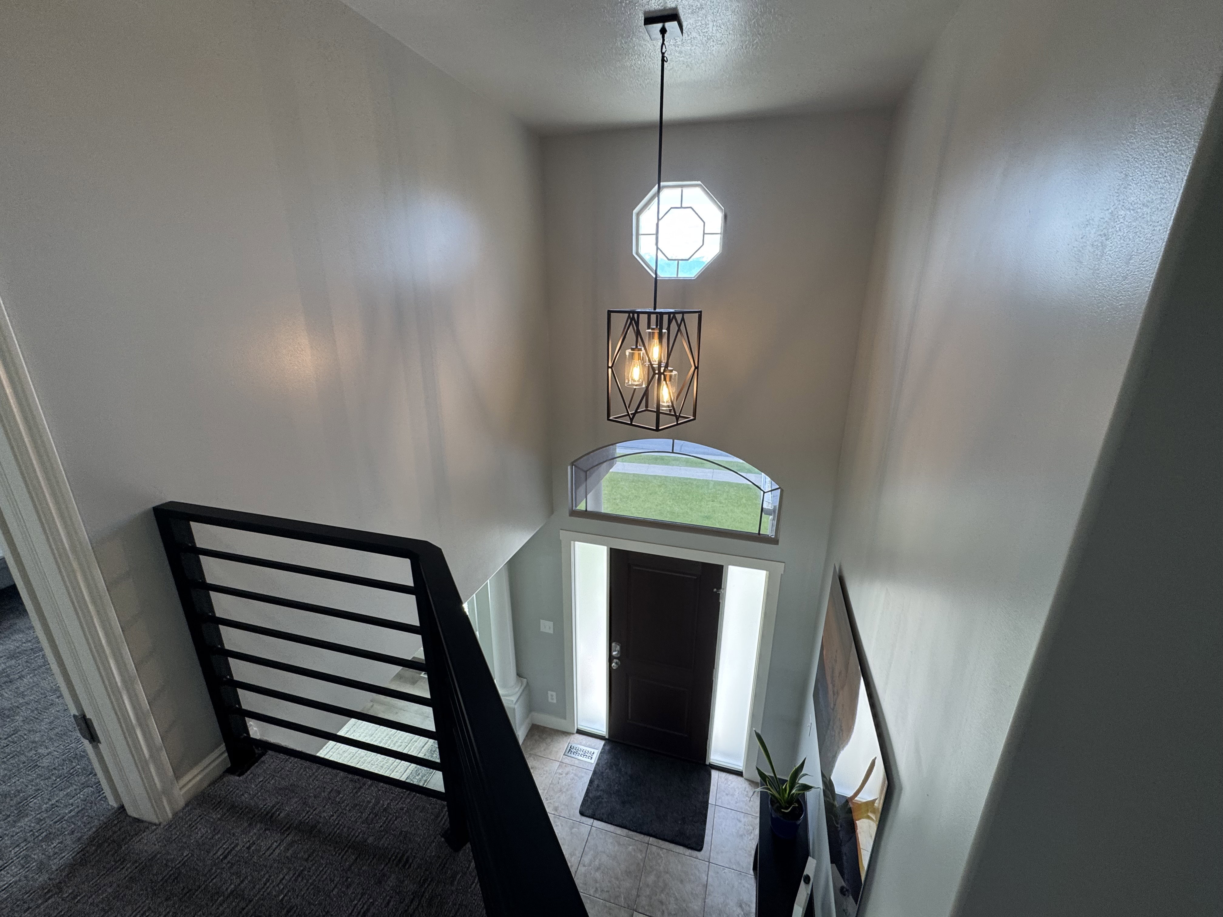Two-story foyer with a modern black geometric chandelier, arched transom window, and an octagonal upper window