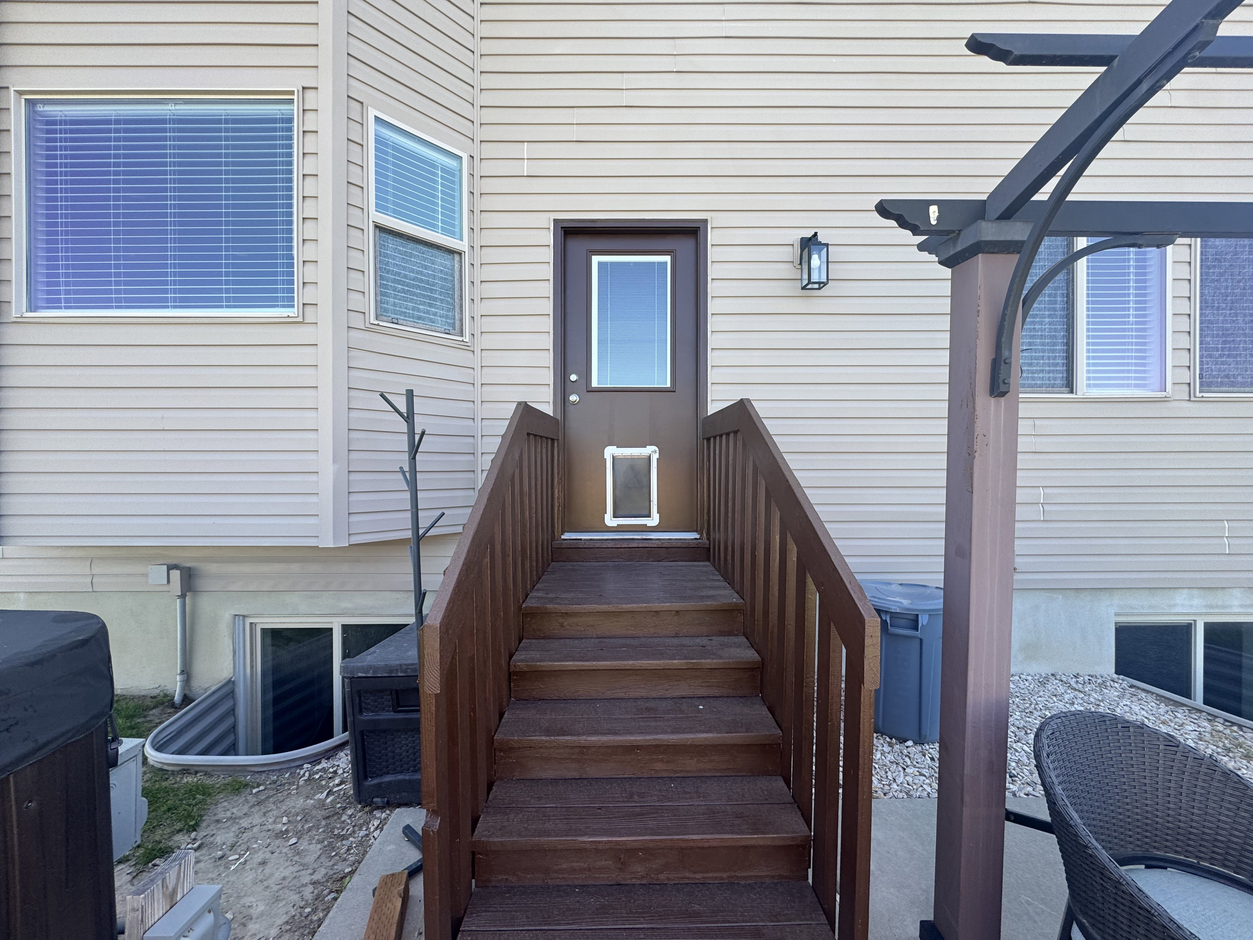 Exterior deck stairs with wood-finish railing leading to a brown door with clear glass panel