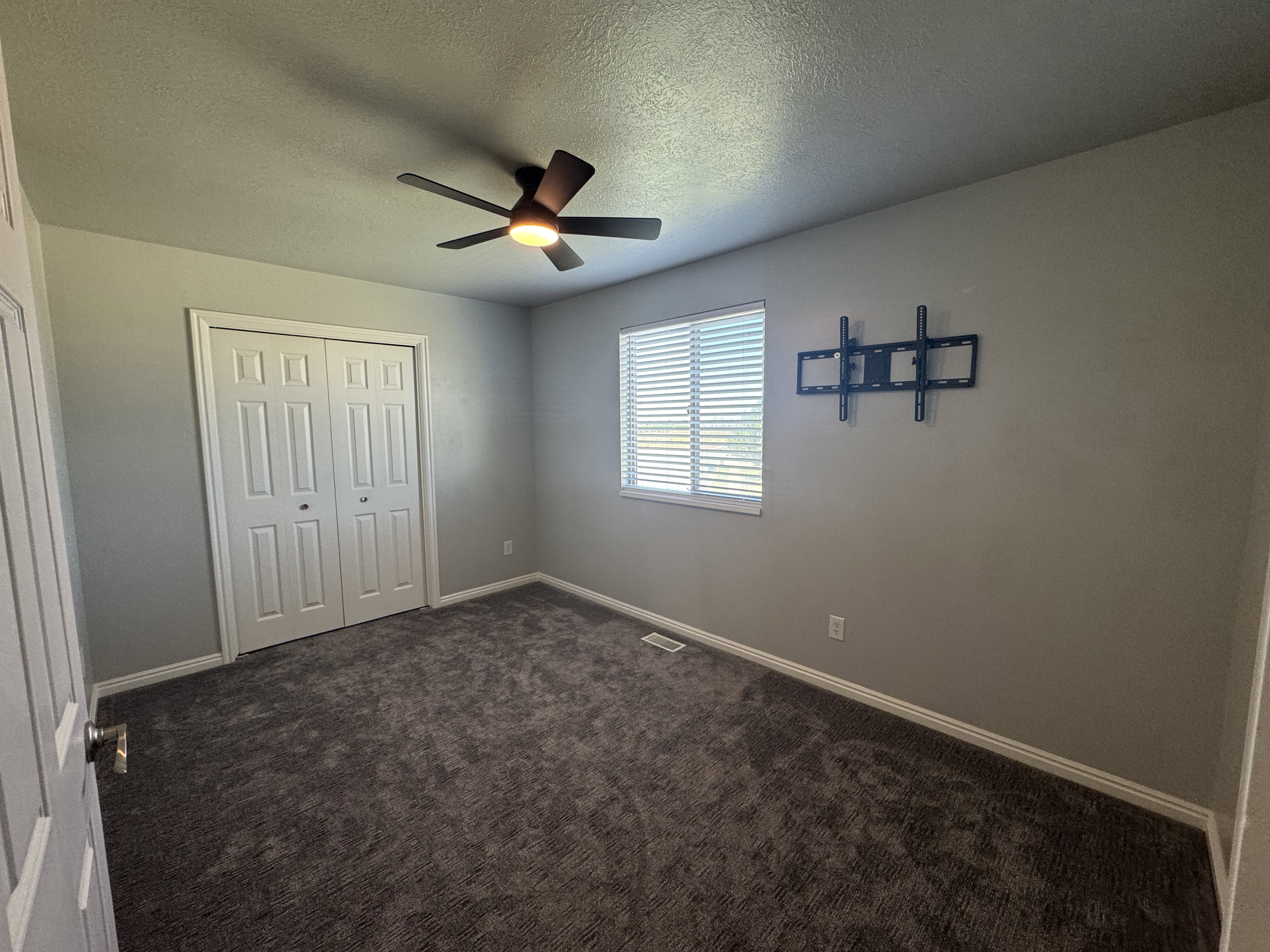 Spacious room featuring neutral-toned walls, textured carpeting, and a ceiling fan with integrated lighting