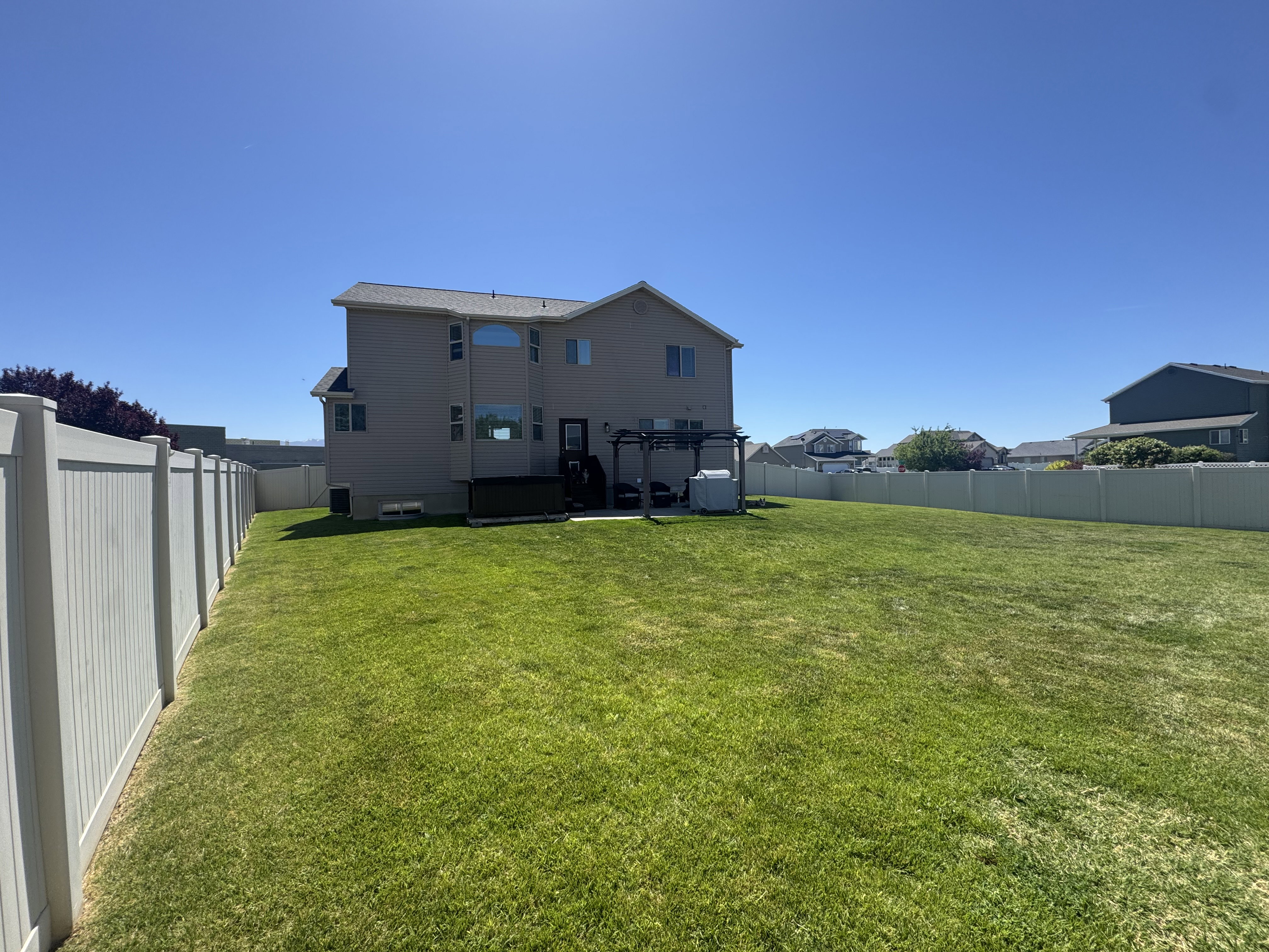 Expansive backyard featuring a lush lawn, privacy fencing, and a two-story residence with multiple windows
