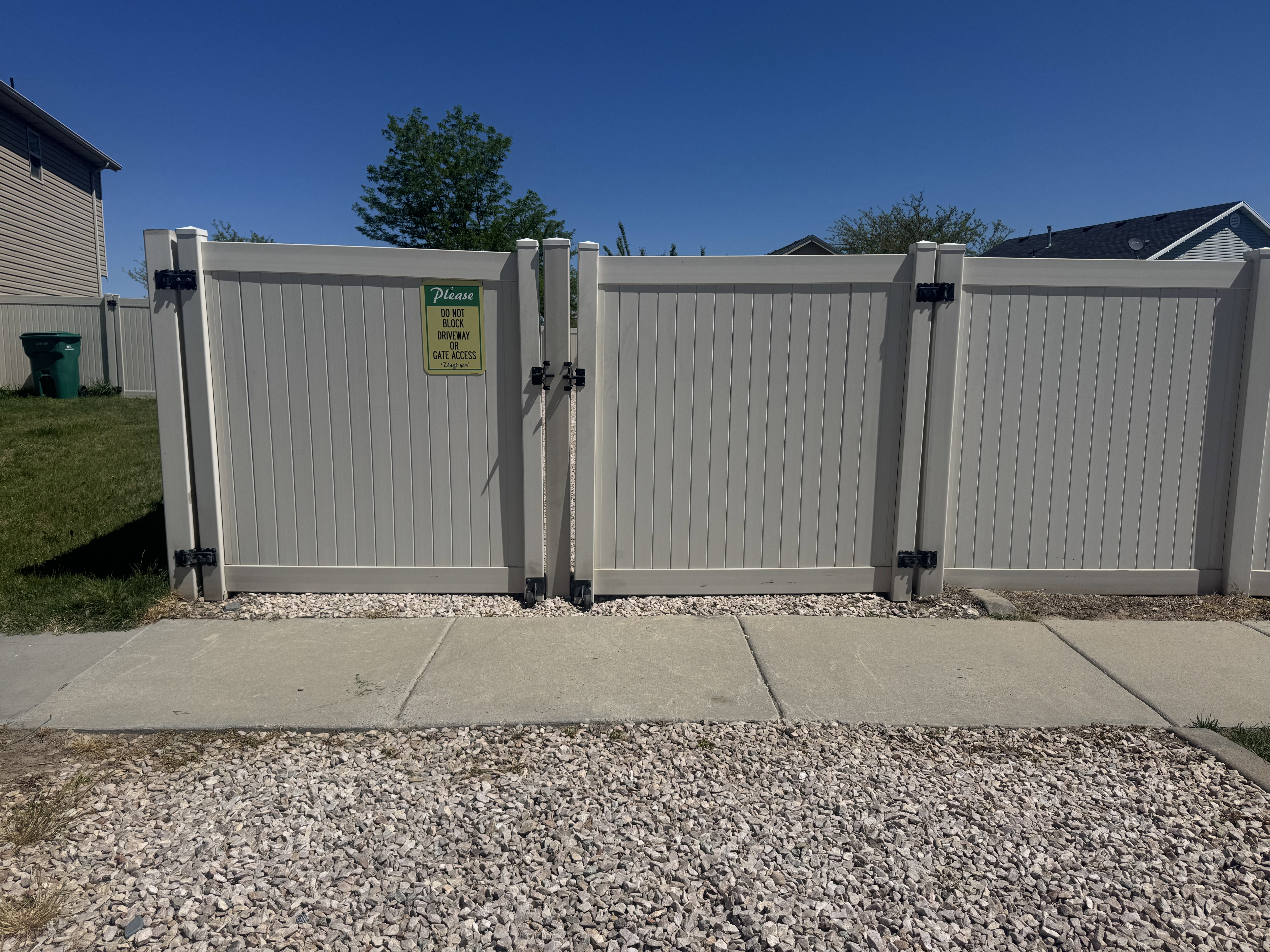 Double-gated PVC fence entry with black hardware, complementing the concrete walkway and gravel ground cover