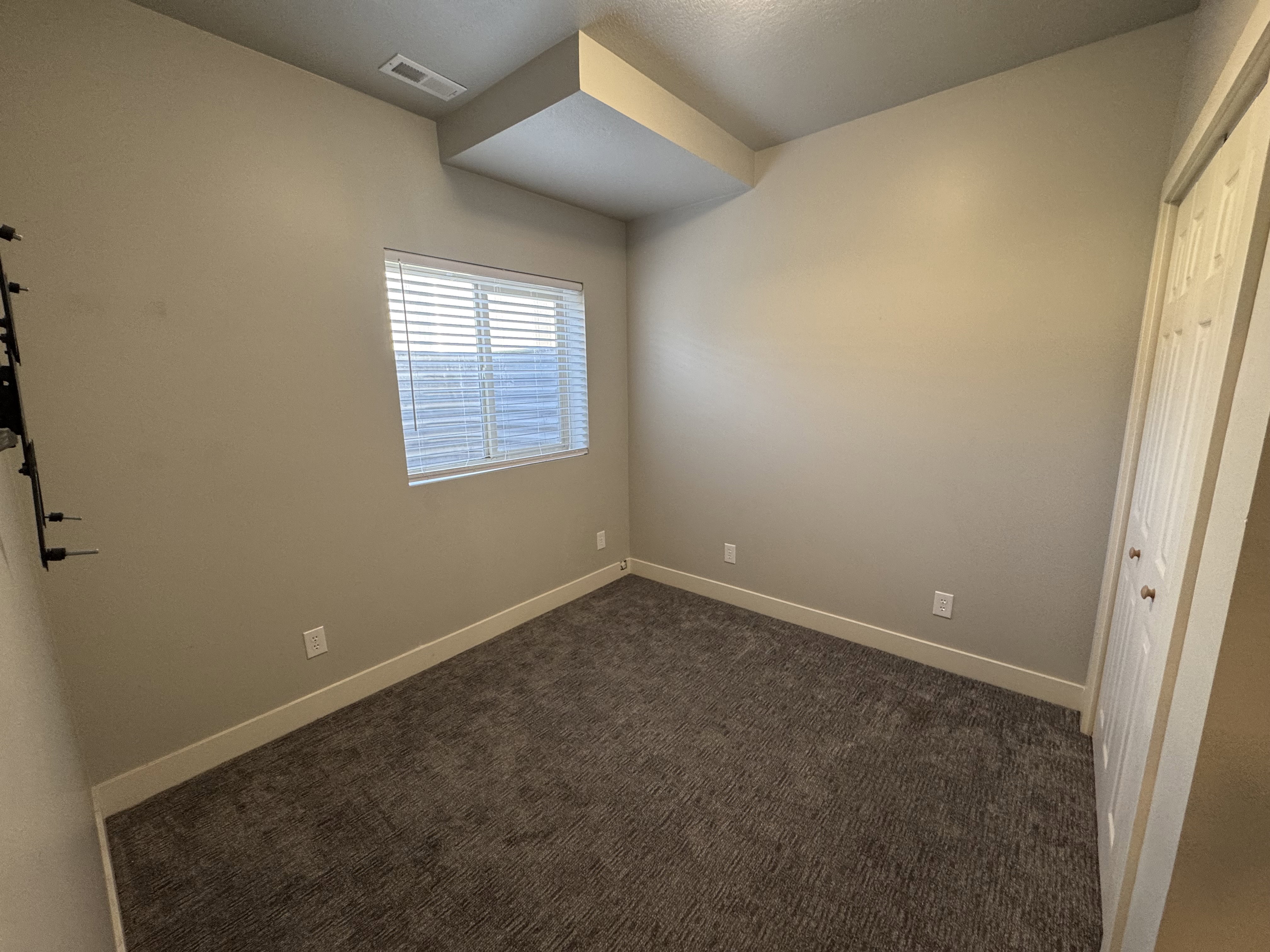Neutral-toned walls and plush carpet flooring complement a window with blinds