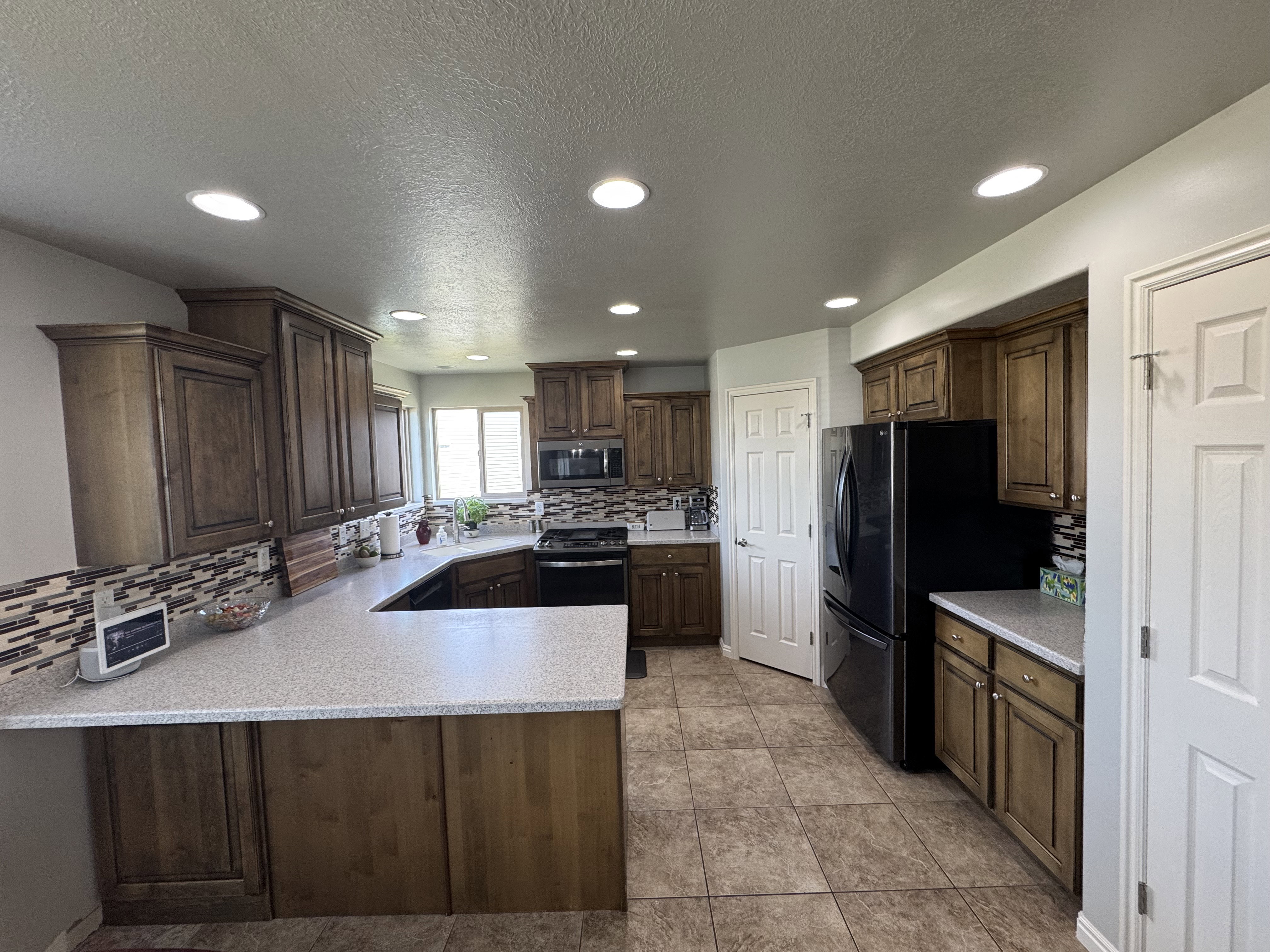 U-shaped kitchen featuring warm wood cabinetry, textured backsplash, light speckled countertops, and tile flooring