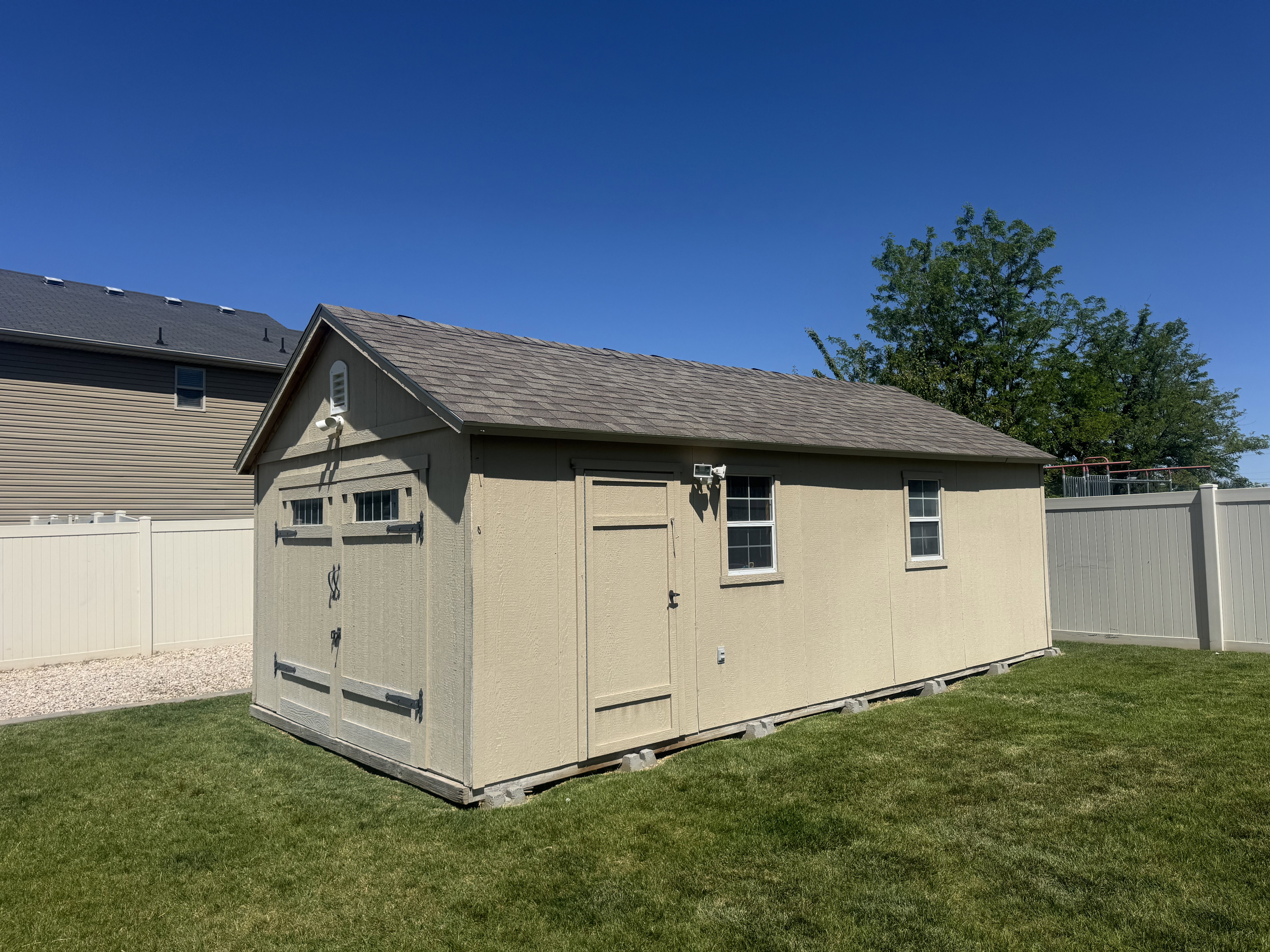 Spacious detached shed featuring an asphalt shingle roof, double-door access, side entry door, and two windows