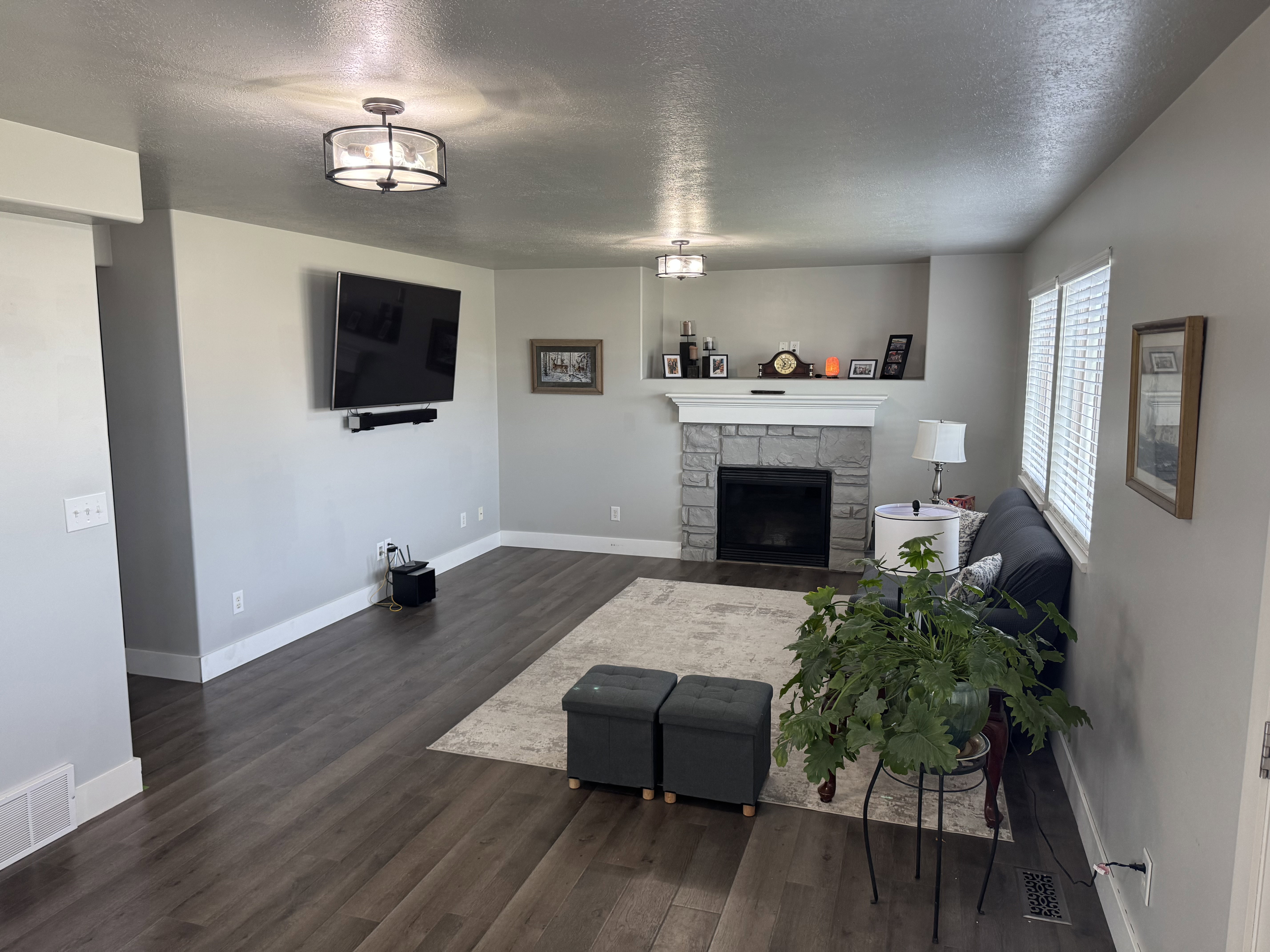Spacious living area featuring wood-finish flooring, a stone-surround fireplace with white mantel, recessed shelving, and two ceiling-mounted light fixtures