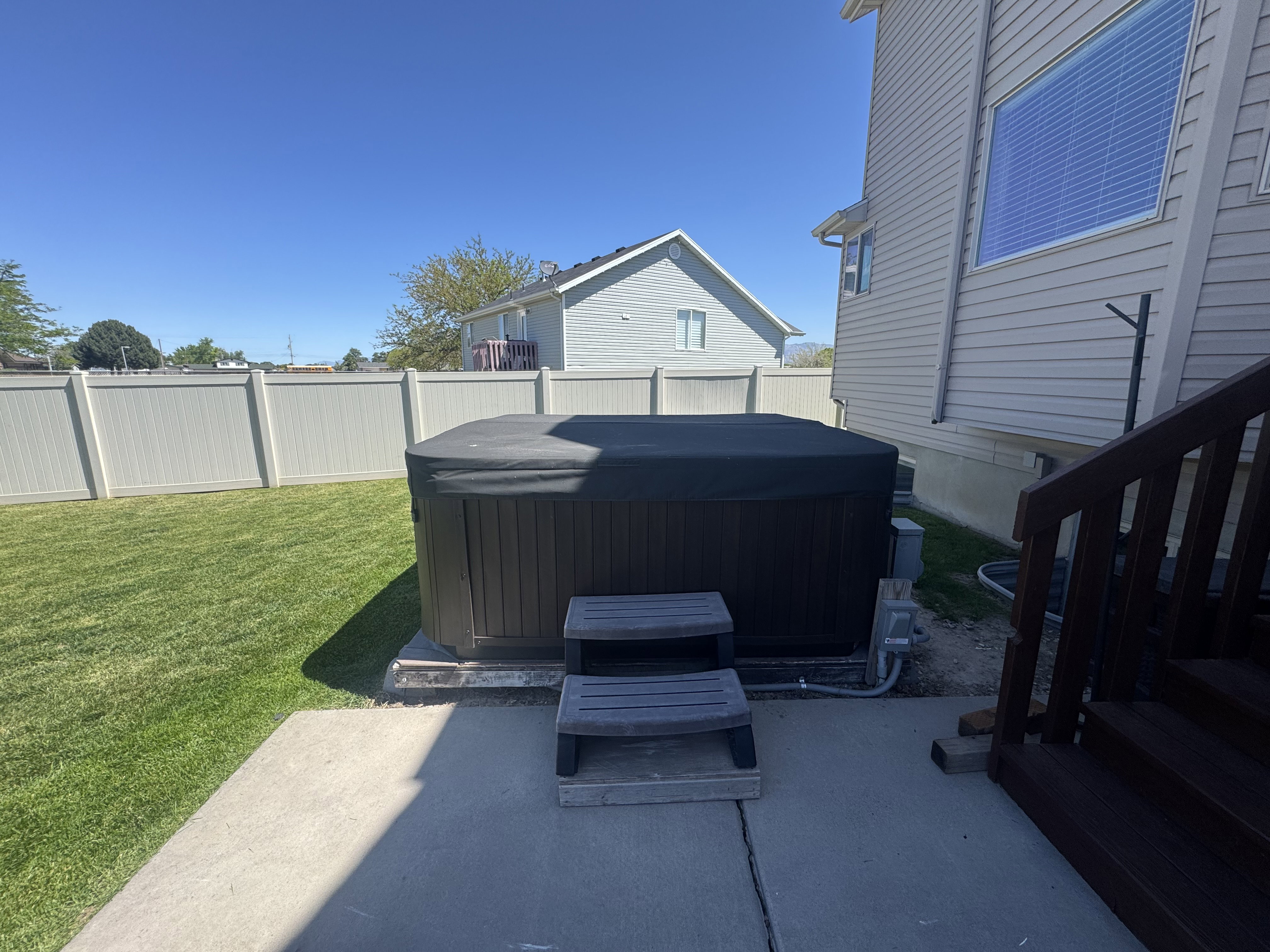 Private backyard featuring a covered hot tub, concrete patio, and a manicured lawn