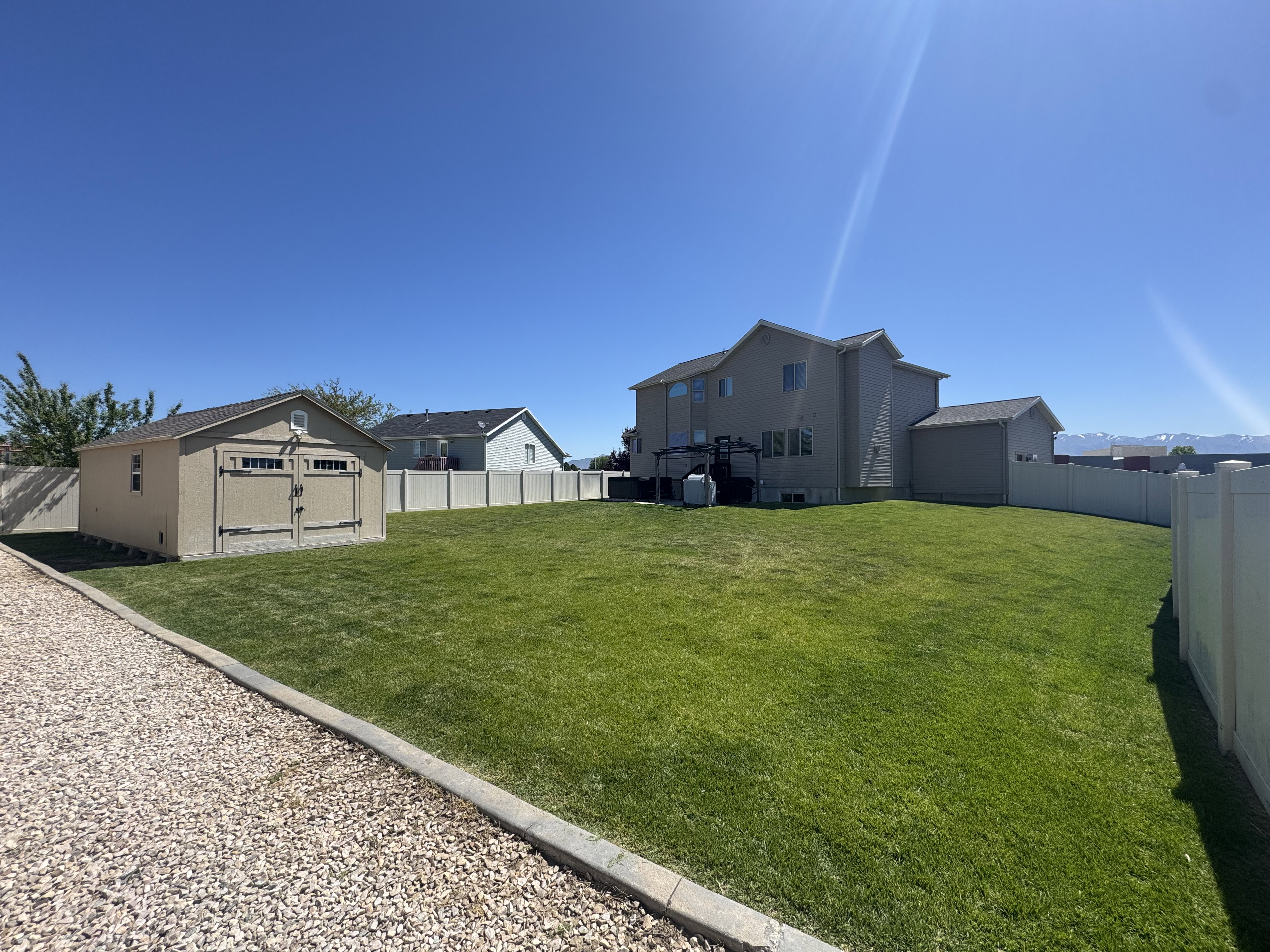 Expansive backyard featuring a large green lawn, a detached storage shed with double doors, and a light-colored vinyl privacy fence