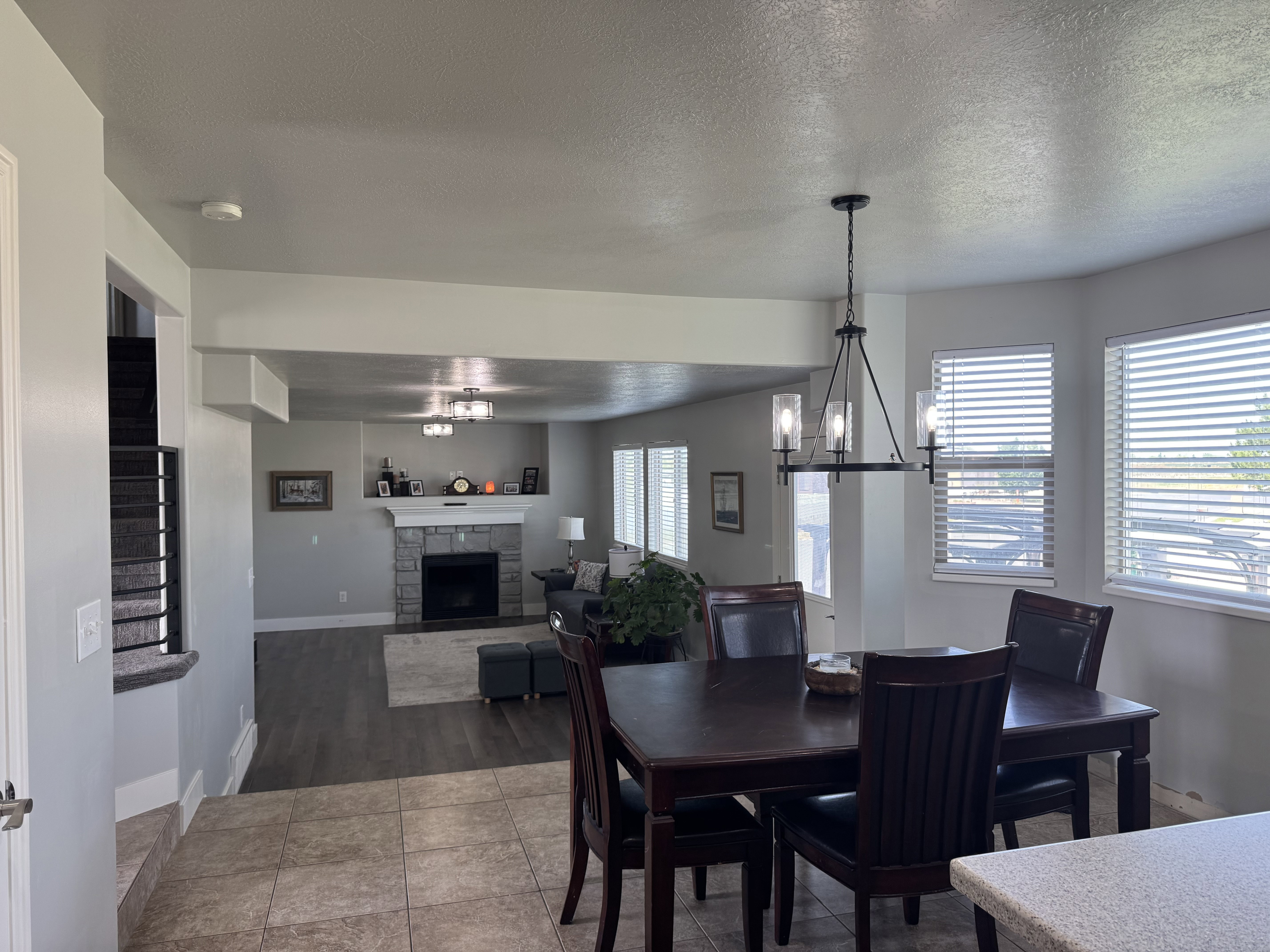 Combined dining and living area featuring a stone-faced fireplace with a white mantel, dark wood-finish flooring in the living space, and light-toned tile flooring in the dining area