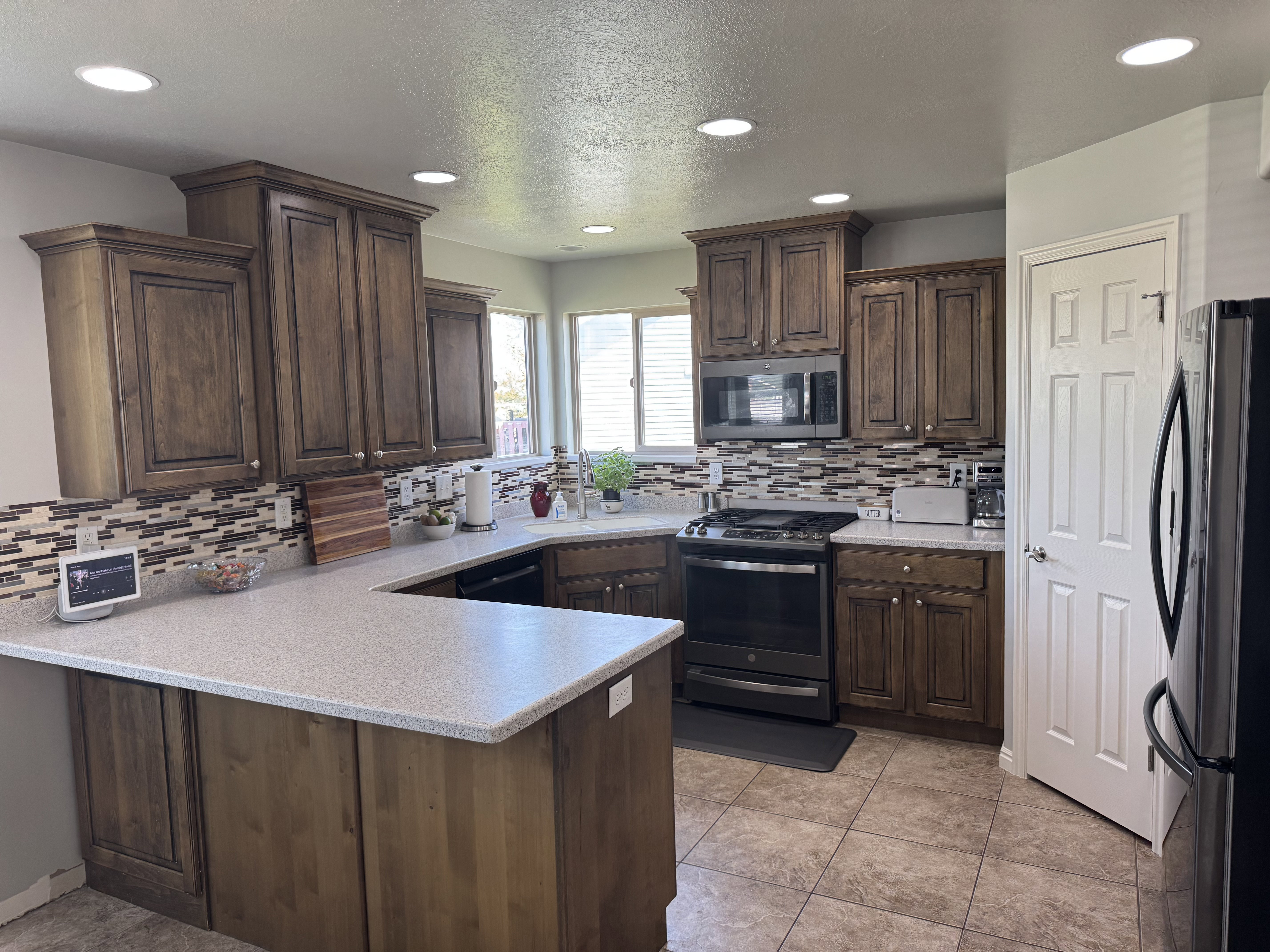 U-shaped kitchen featuring wood cabinetry, light-colored countertops, and a mosaic tile backsplash