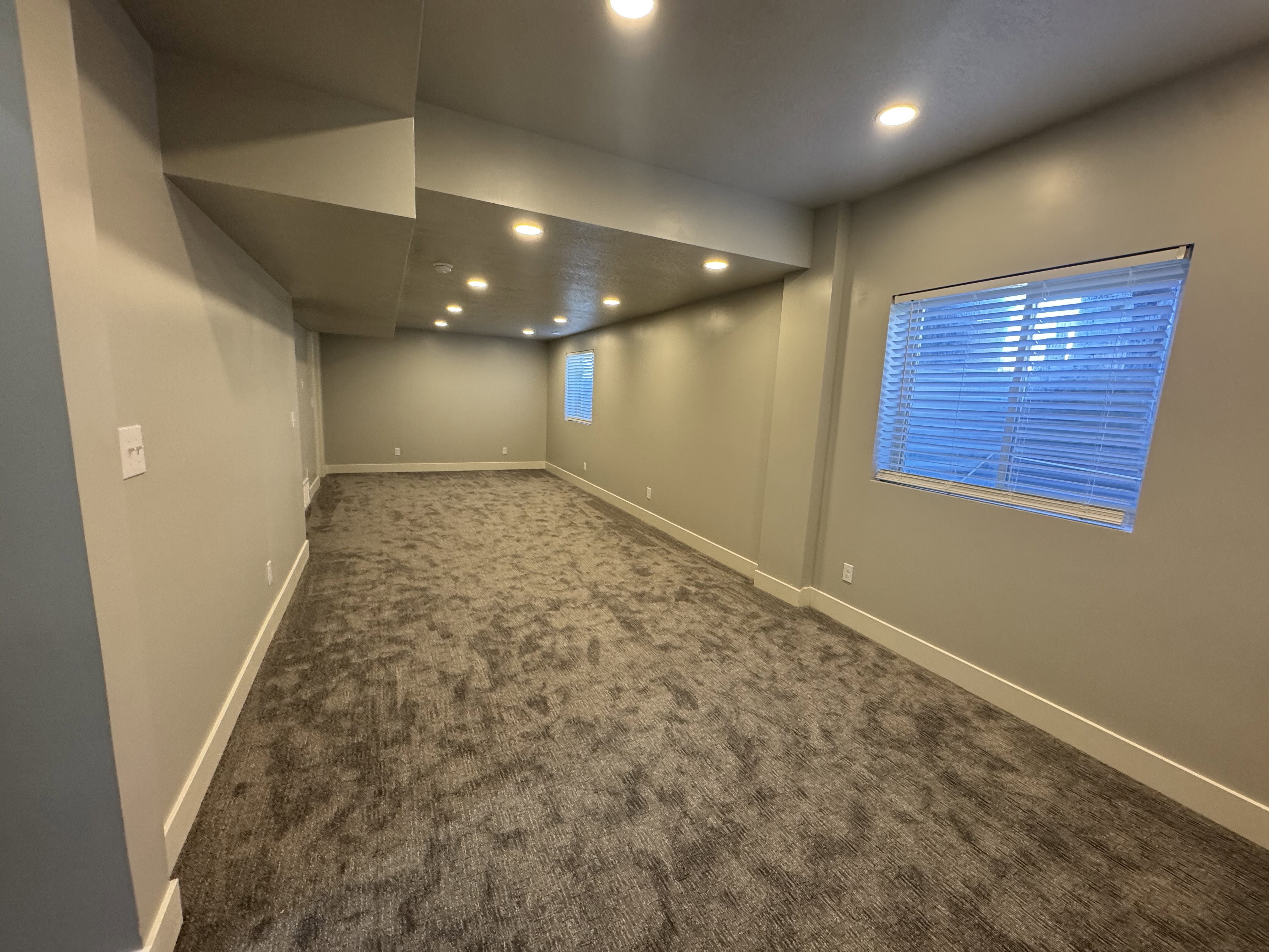 Spacious room featuring neutral-toned walls, recessed lighting, and patterned carpet flooring