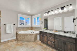 Spacious bathroom featuring a corner soaking tub with tile surround, dual windows with louvered shutters, a large double vanity with granite-style countertop, and tile flooring