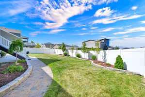 Expansive backyard featuring a lush lawn, white privacy fencing, and a paver stone walkway