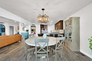 Open-concept living space with wood-finish flooring, a contemporary chandelier, recessed lighting, white crown molding, and a kitchen featuring dark wood cabinetry and granite countertops