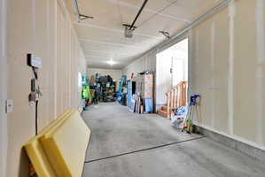 Spacious garage with concrete flooring, unfinished drywall, and exposed ceiling joists