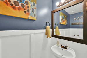 Pedestal sink with bronze-finish faucet, dark wood-frame mirror, and three-bulb vanity light fixture