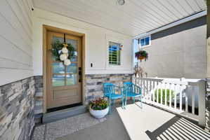Covered front porch featuring a wood-finish entry door with clear glass panels, horizontal siding, stone veneer accents, white railing, and a concrete floor