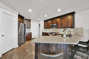 Kitchen featuring wood-finish flooring, dark wood cabinetry, stainless steel appliances, and granite countertops with a subway tile backsplash