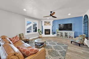 Spacious living area featuring a corner fireplace with a white mantel, wood-finish flooring, recessed lighting, and a ceiling fan