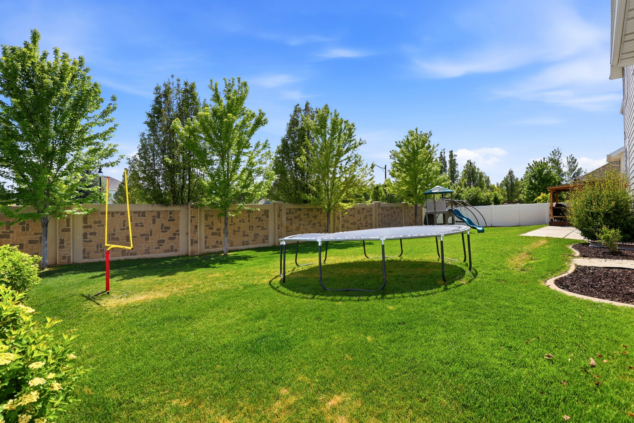 Expansive green lawn with mature trees and a patterned privacy fence