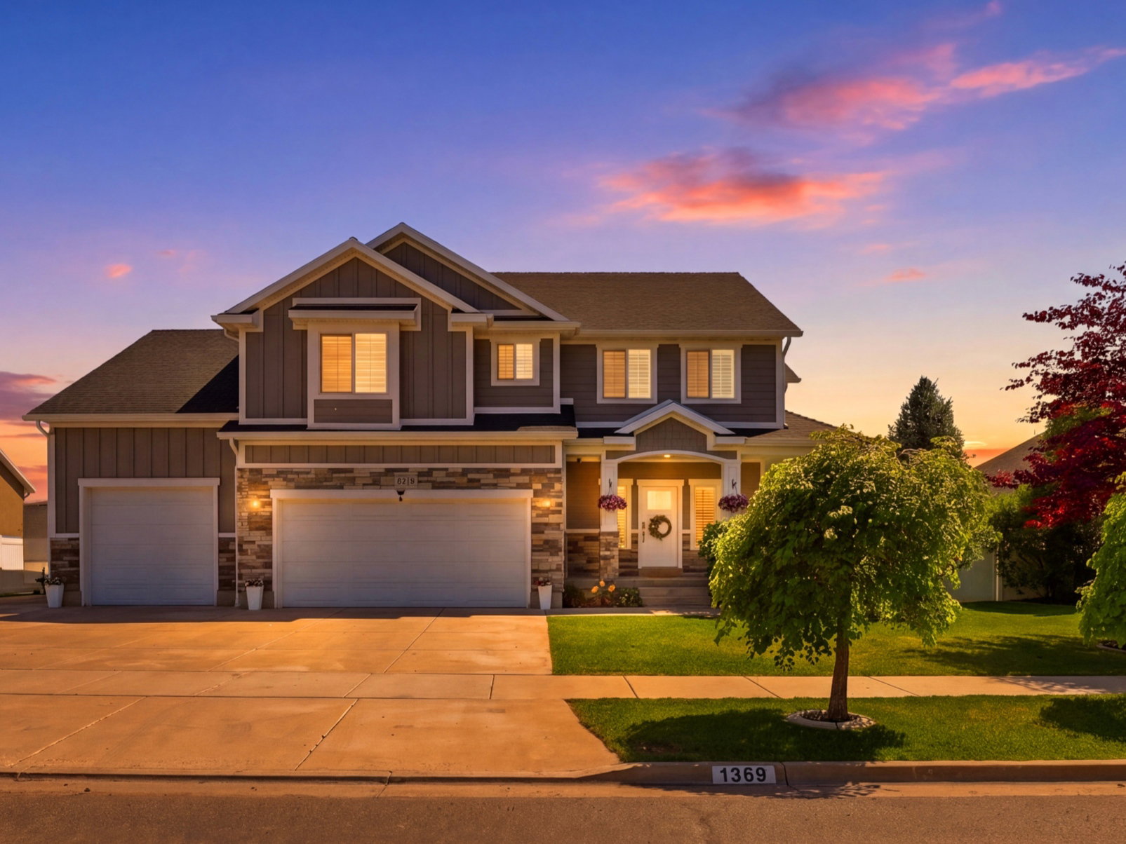 Two-story residence featuring a dual garage, stone facade accents, and a well-maintained lawn with mature trees