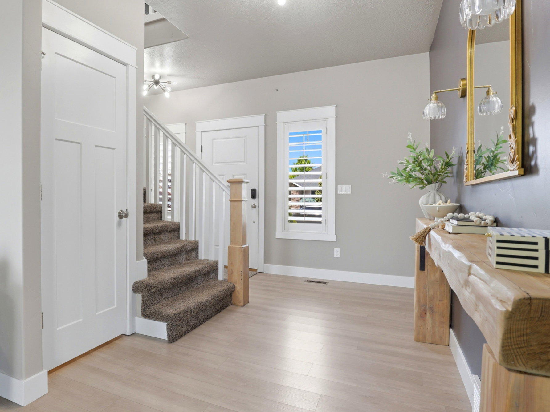 Entryway featuring light wood-finish flooring, a carpeted staircase with white railings, and a window with white louvered shutters