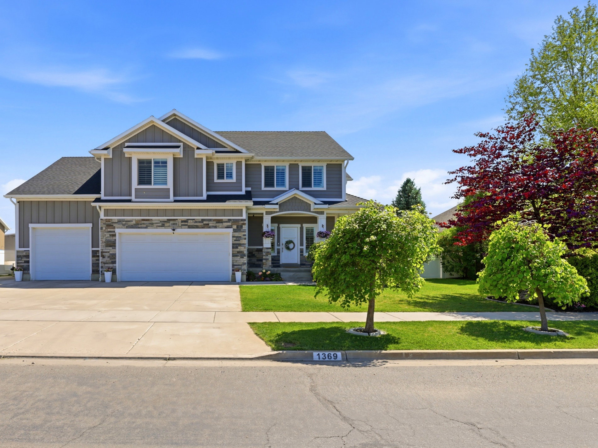 Two-story residence featuring a gray siding and stone facade, a covered front entry, a two-car garage, and a concrete driveway