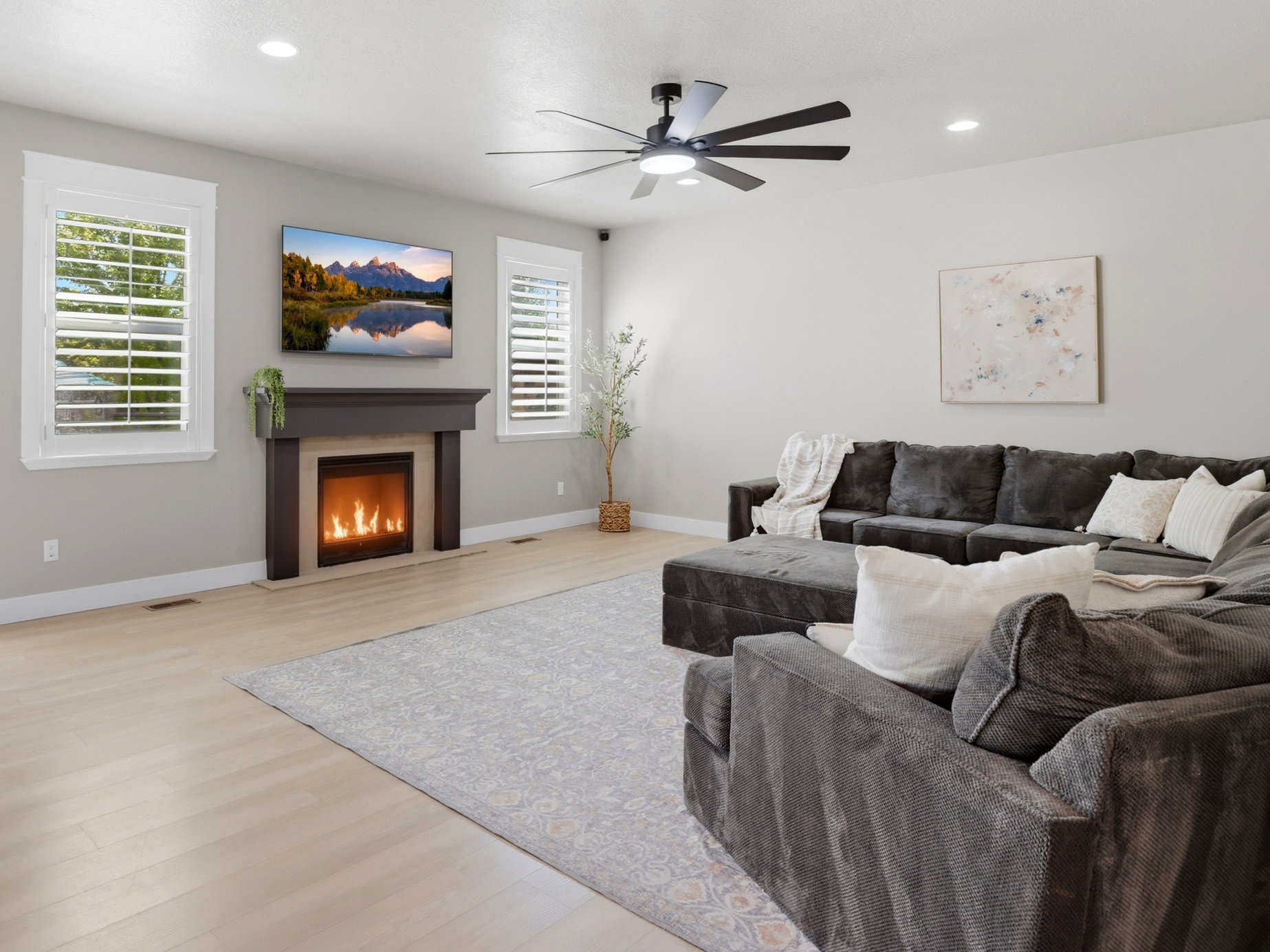 Spacious living area featuring a modern fireplace with a dark wood mantel, light wood-finish flooring, and recessed lighting