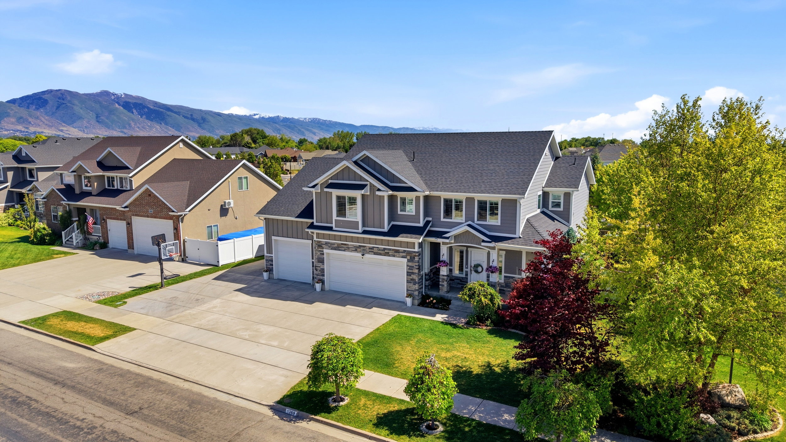 Two-story residence featuring a gray siding and stone exterior, a dark shingle roof, an attached two-car garage, and established front yard landscaping