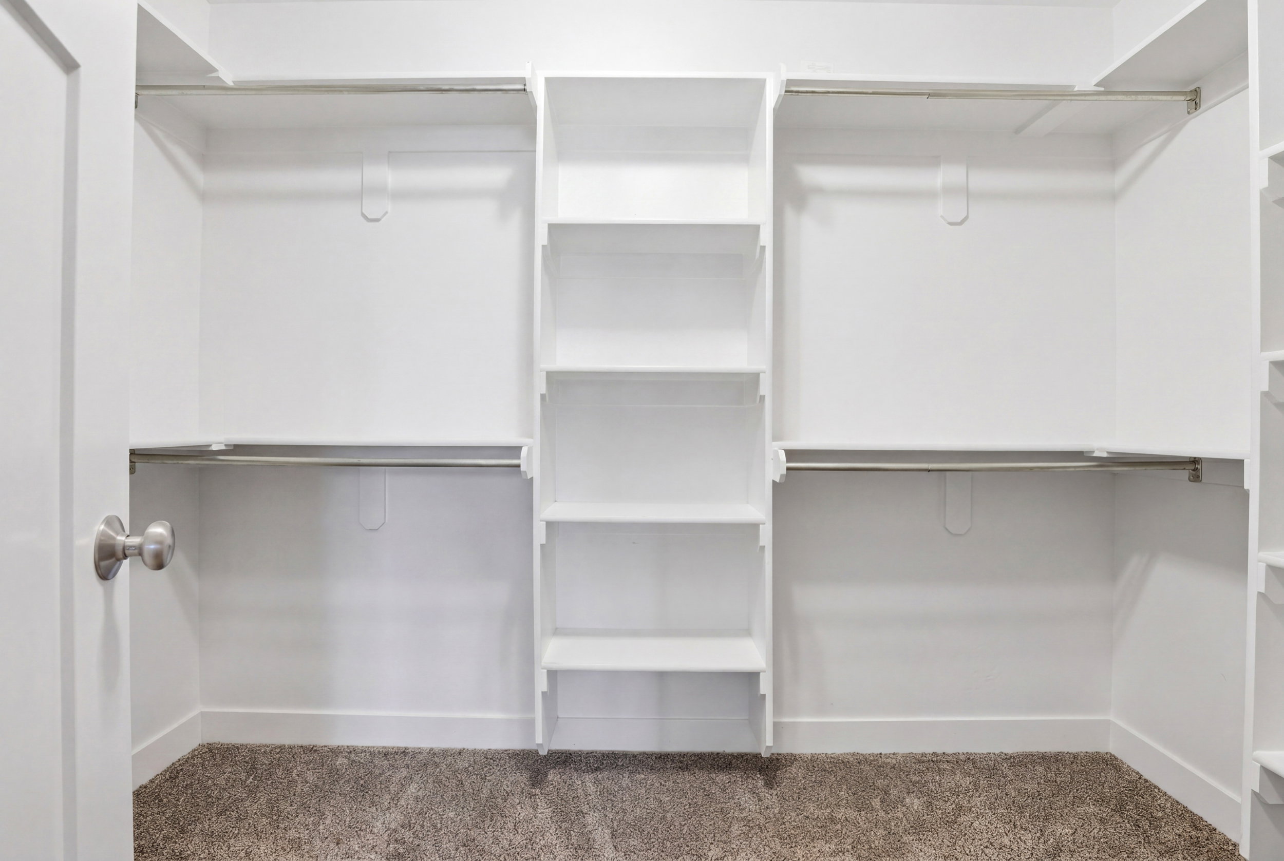 Custom closet system with white shelving, multiple hanging rods, and integrated shelving units