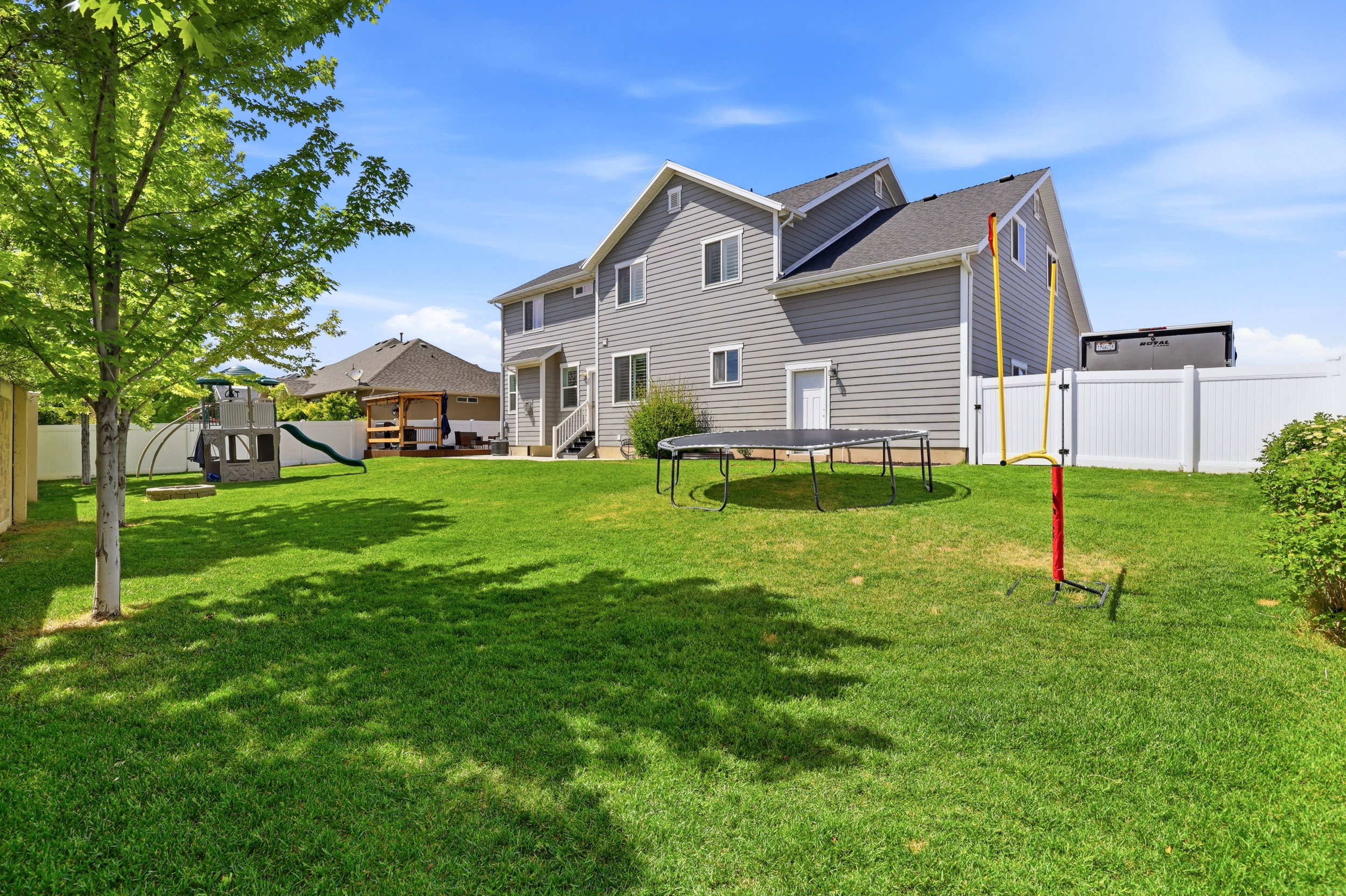 Expansive backyard featuring a manicured lawn, established tree, and a white privacy fence