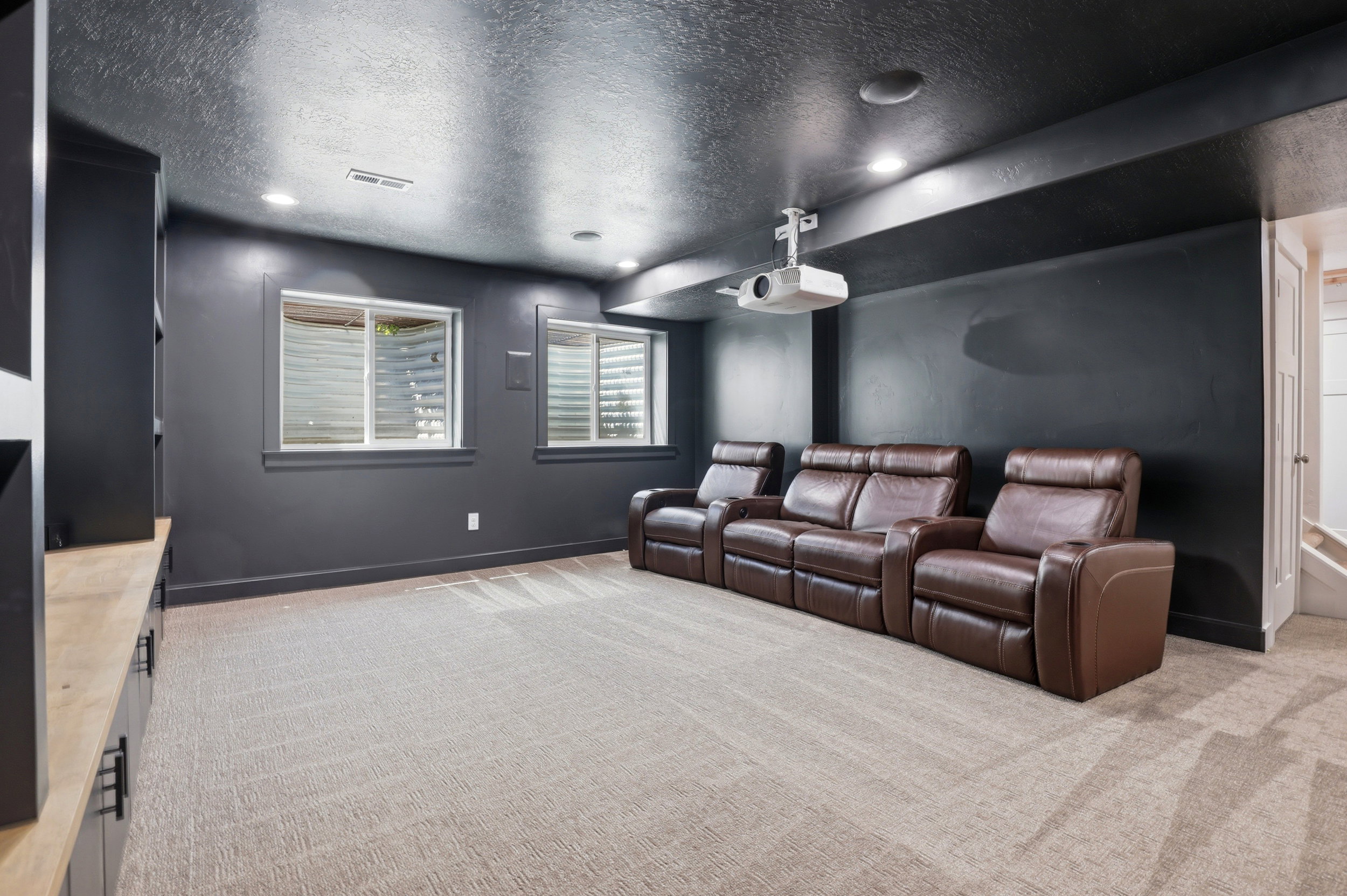 Dedicated media space featuring recessed lighting, a ceiling-mounted projector, and dual egress windows with blinds