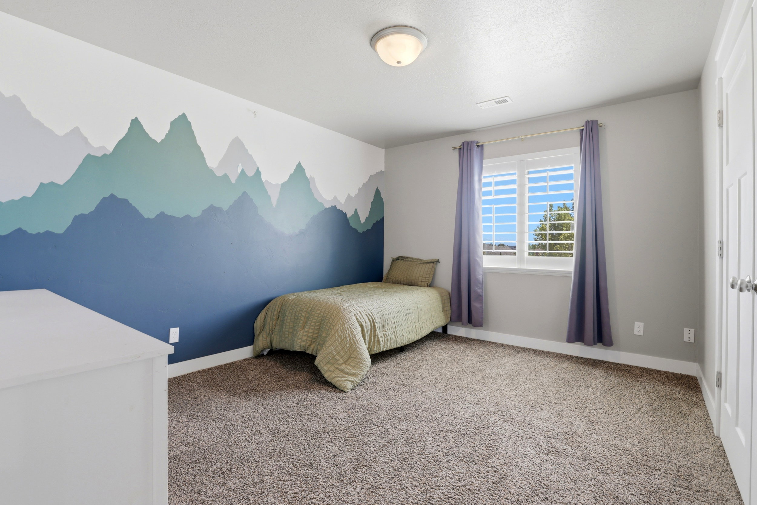 Feature wall with mountain mural, white plantation shutters, neutral carpeting, white trim, and a semi-flush mount ceiling fixture