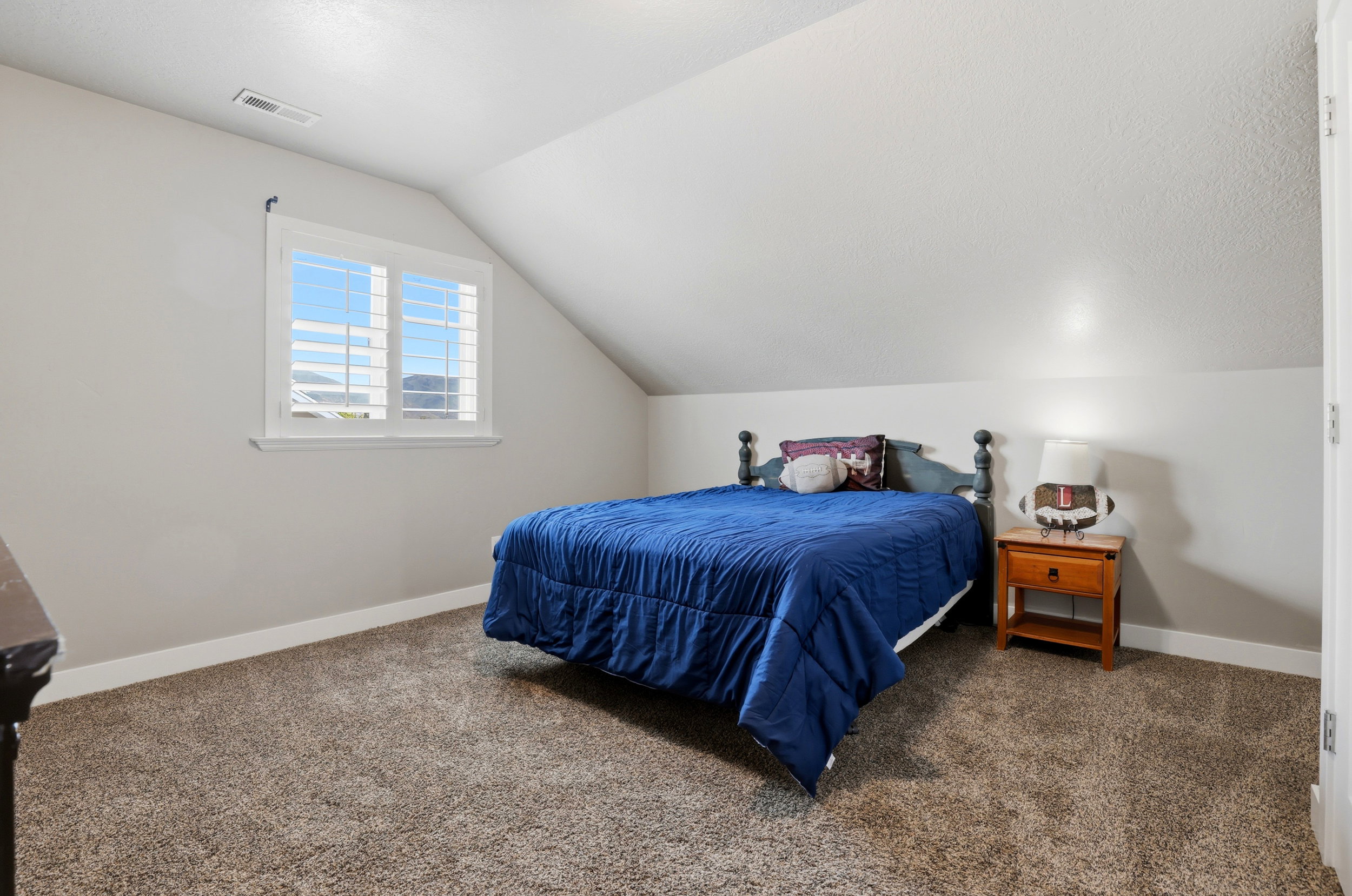 Carpeted room with an angled ceiling and a single window featuring white plantation shutters