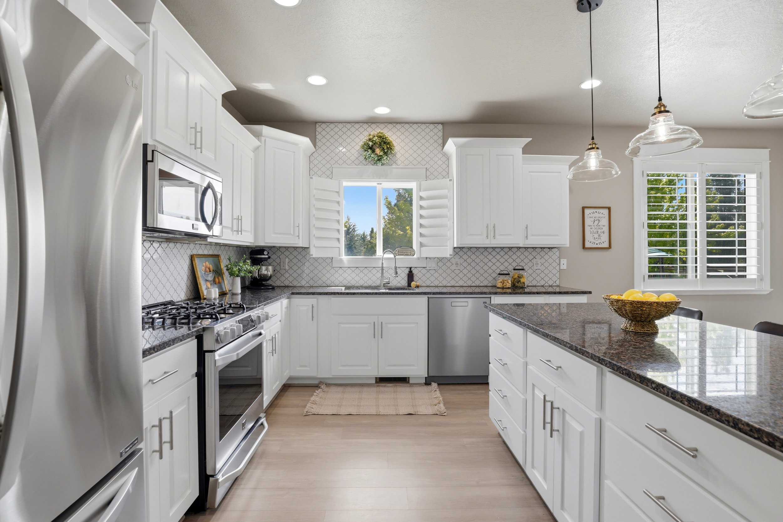 Bright kitchen featuring white cabinetry, stainless steel appliances, dark stone countertops, diamond-patterned backsplash, and wood-finish flooring