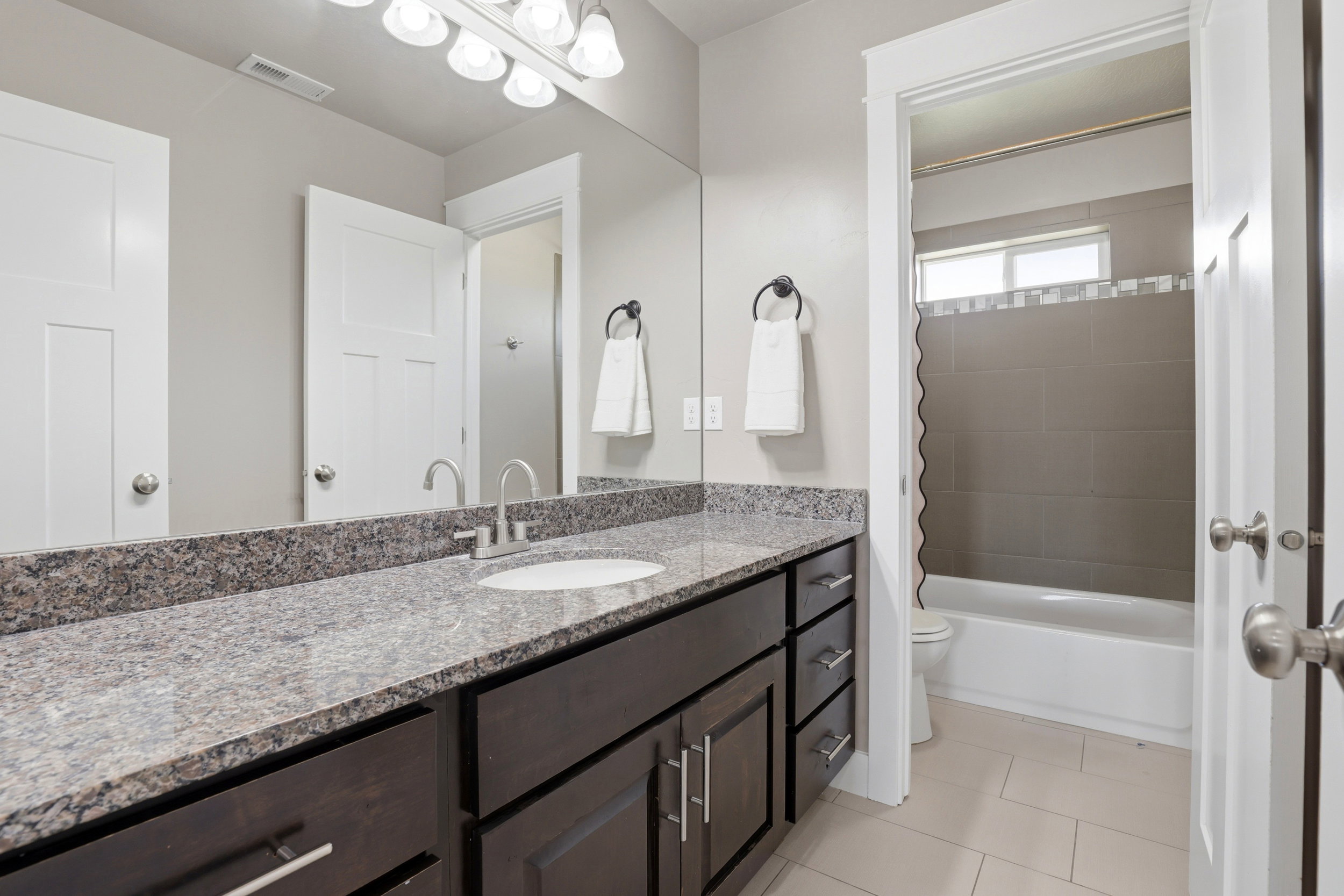 Bathroom featuring a dark wood-finish vanity with ample storage, a granite countertop, and a single undermount sink