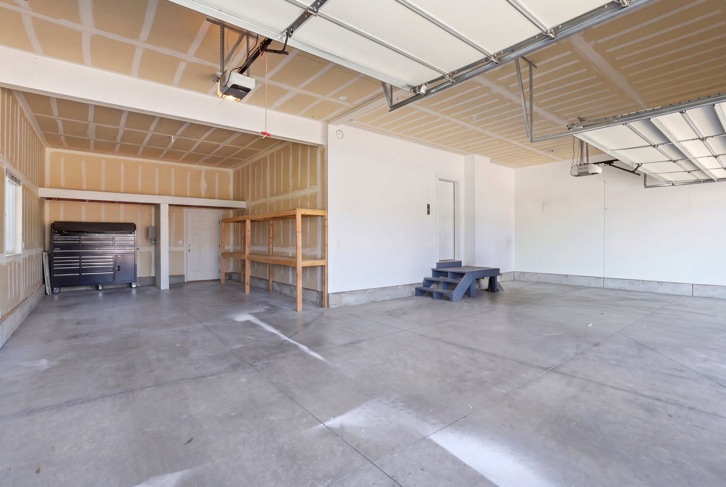 Spacious garage featuring a concrete floor, overhead garage door with opener, and built-in wooden shelving for storage