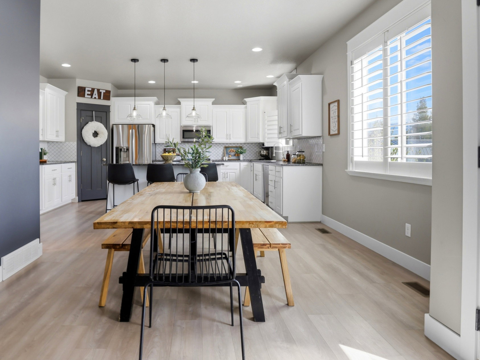 Open-concept dining area with wood-finish flooring, recessed lighting, and a window with white plantation shutters