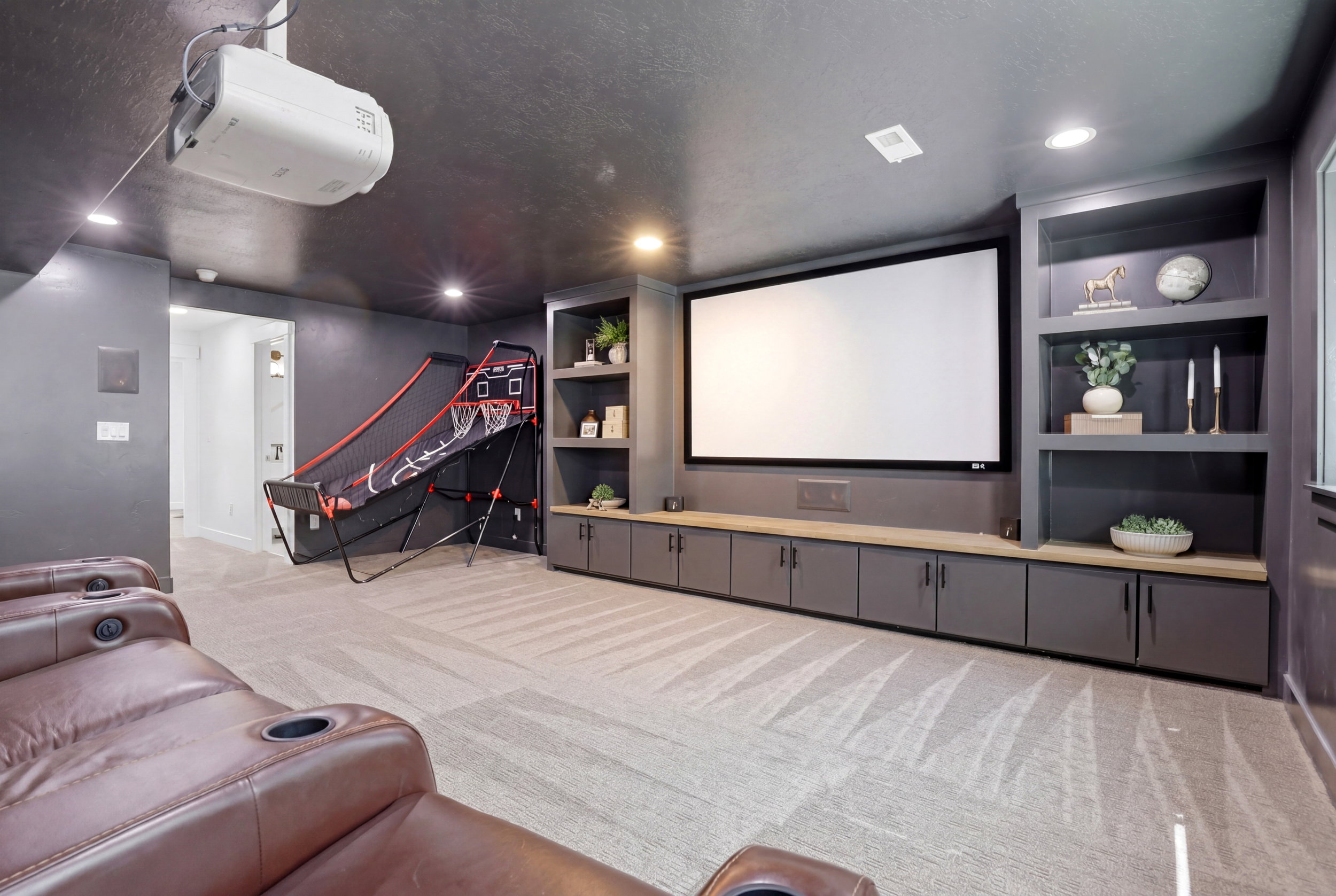Dedicated media room featuring a large projection screen, built-in cabinetry with wood-finish countertops, recessed lighting, and integrated shelving