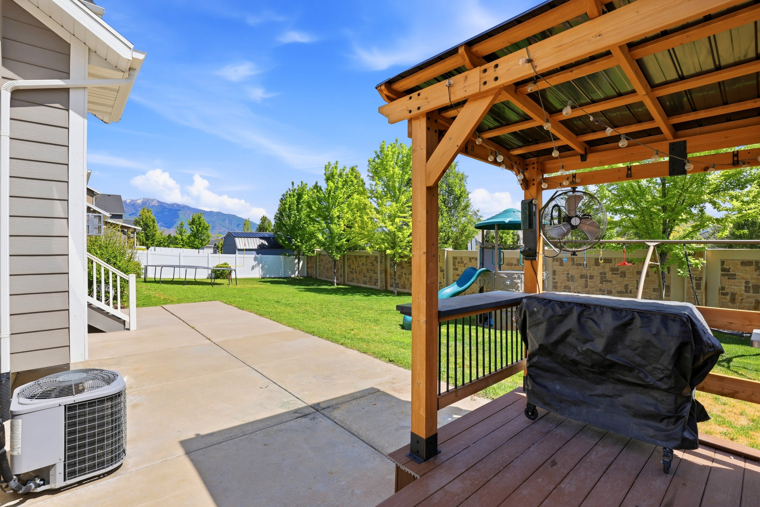 Expansive backyard featuring a wood pergola with string lights, a concrete patio, a large grass lawn, and wood privacy fencing