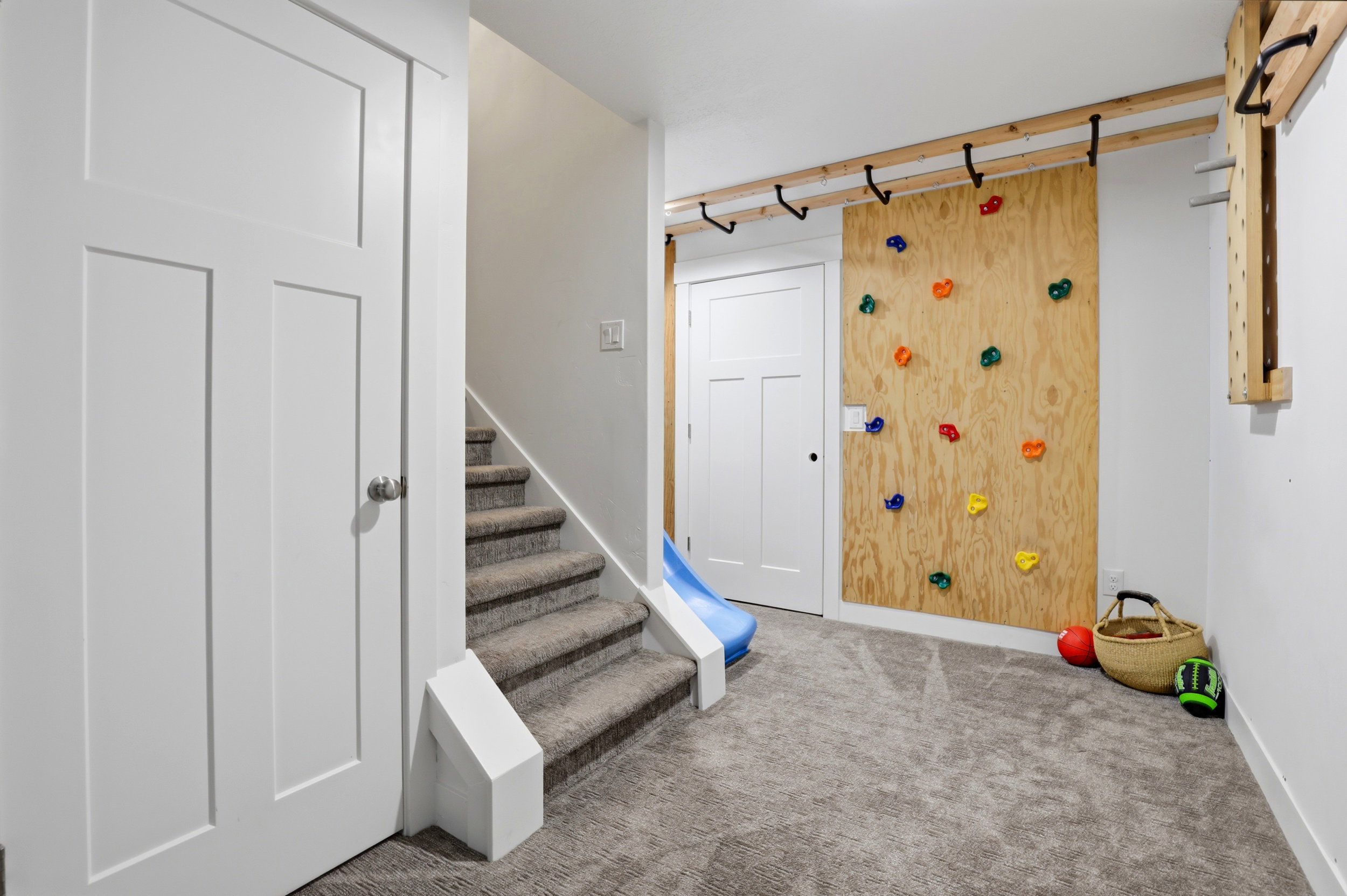 Recreational room featuring a built-in climbing wall with colorful holds, a wooden ladder, and durable gray carpeting