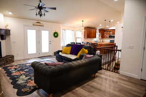 Open-concept living area featuring wood-finish flooring, a ceiling fan with integrated lighting, and white French doors