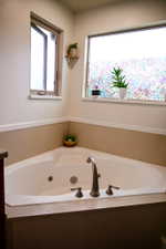 Corner jetted tub featuring a deck-mounted faucet with dual handles