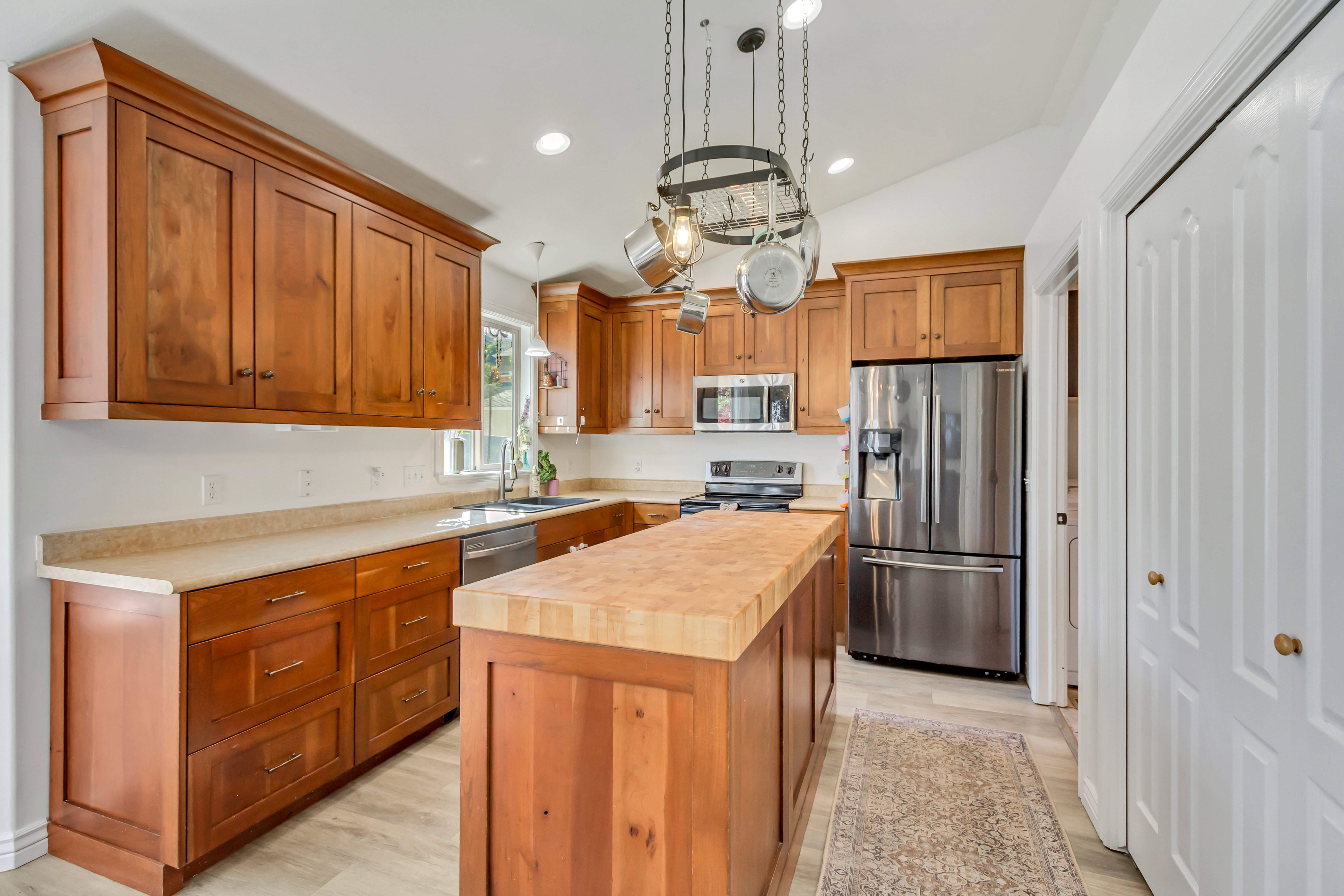Kitchen featuring wood cabinetry, light-toned countertops, stainless steel appliances, a center island with a wood-finish top, and vaulted ceilings