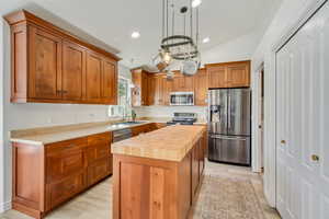 Kitchen featuring wood cabinetry, light-toned countertops, stainless steel appliances, a center island with a wood-finish top, and vaulted ceilings