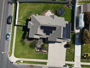 Aerial view showcasing the property with a gray shingle roof, solar panel installation, a concrete driveway, and a fenced backyard