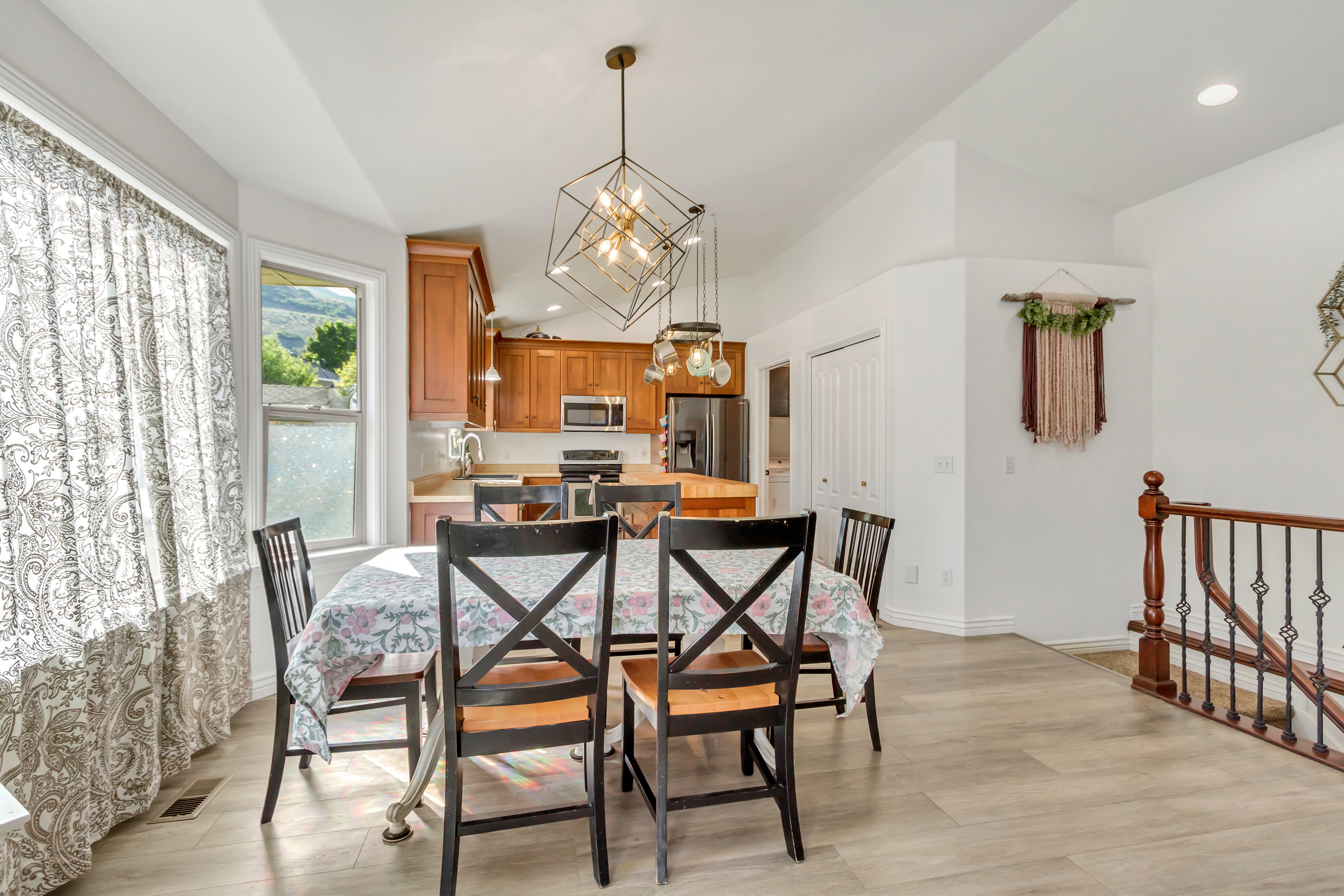 Dining area featuring a contemporary geometric pendant light fixture, wood-finish flooring, and a kitchen with warm-toned cabinetry, stainless steel appliances, and a central island