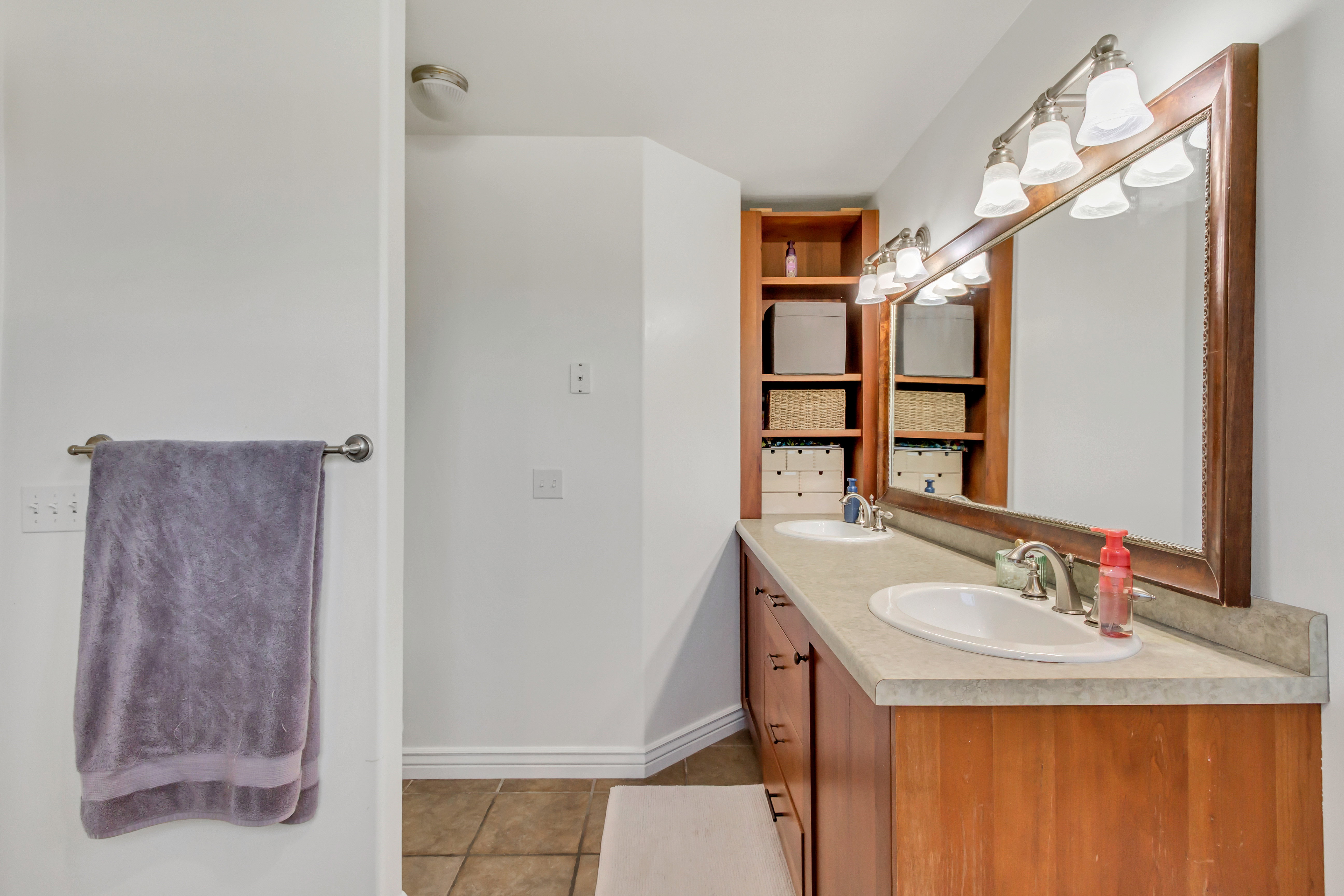 Double vanity with integrated sinks, a wide framed mirror, and warm wood-finish cabinetry