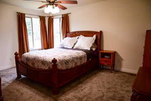 Carpeted room featuring a corner window configuration with drapes, a ceiling fan with integrated lighting, and neutral wall paint