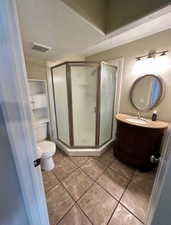 Bathroom featuring a corner shower enclosure with frosted glass, a curved vanity with a basin sink and stone countertop, and tile flooring